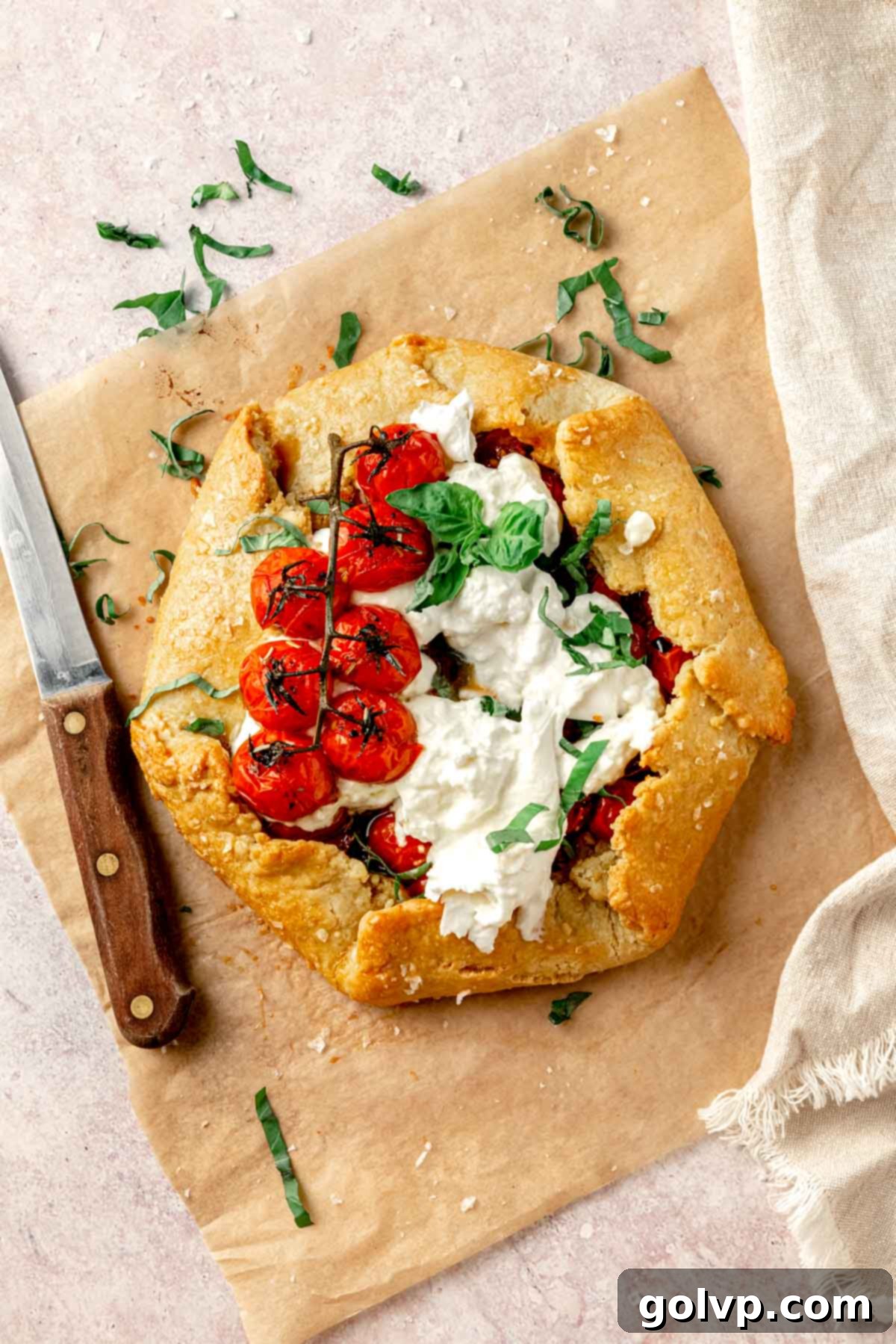 Fully assembled tomato galette with tomatoes, burrata, and basil on parchment paper