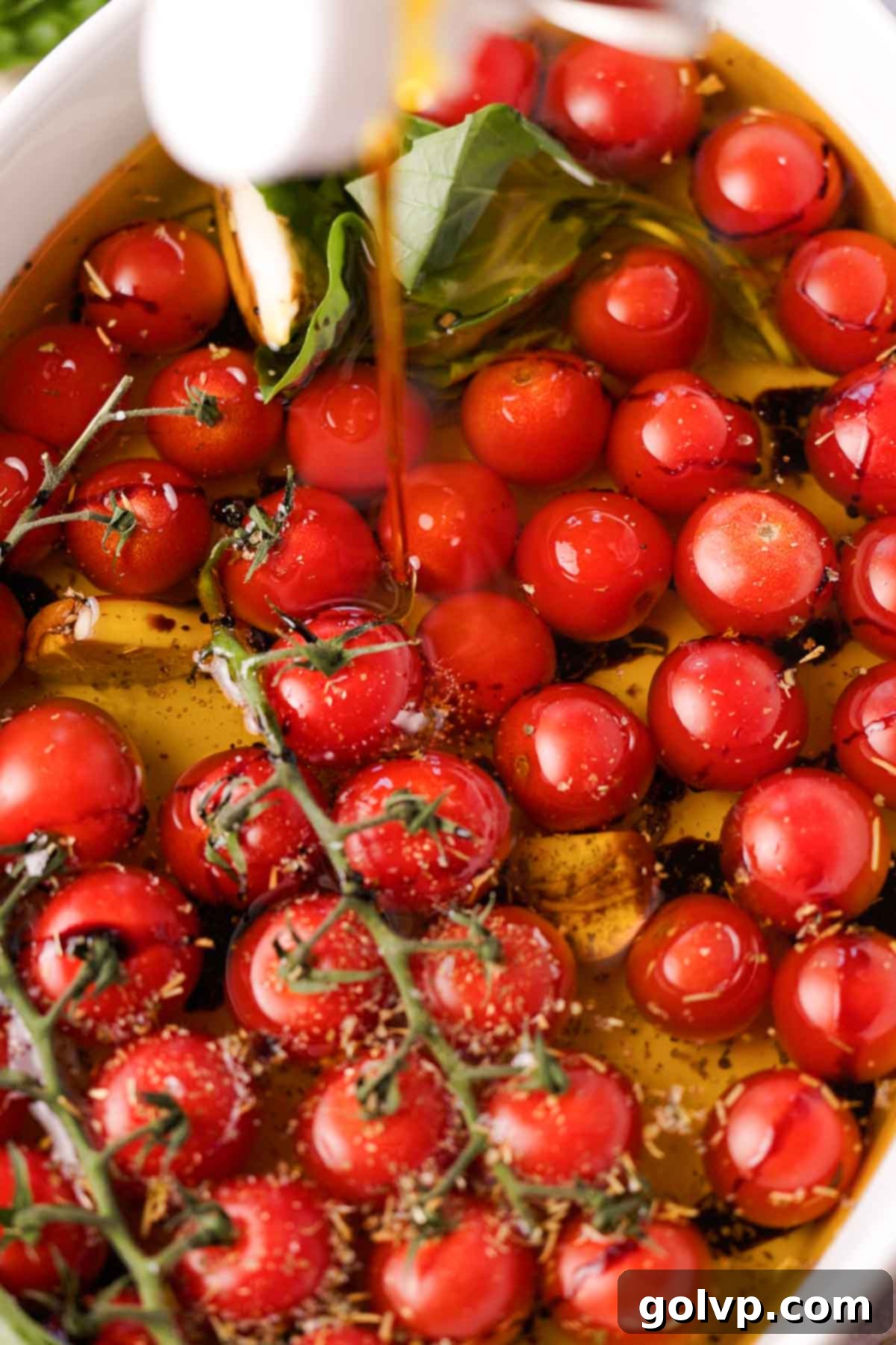 Generously covering cherry tomatoes with extra virgin olive oil in a baking dish