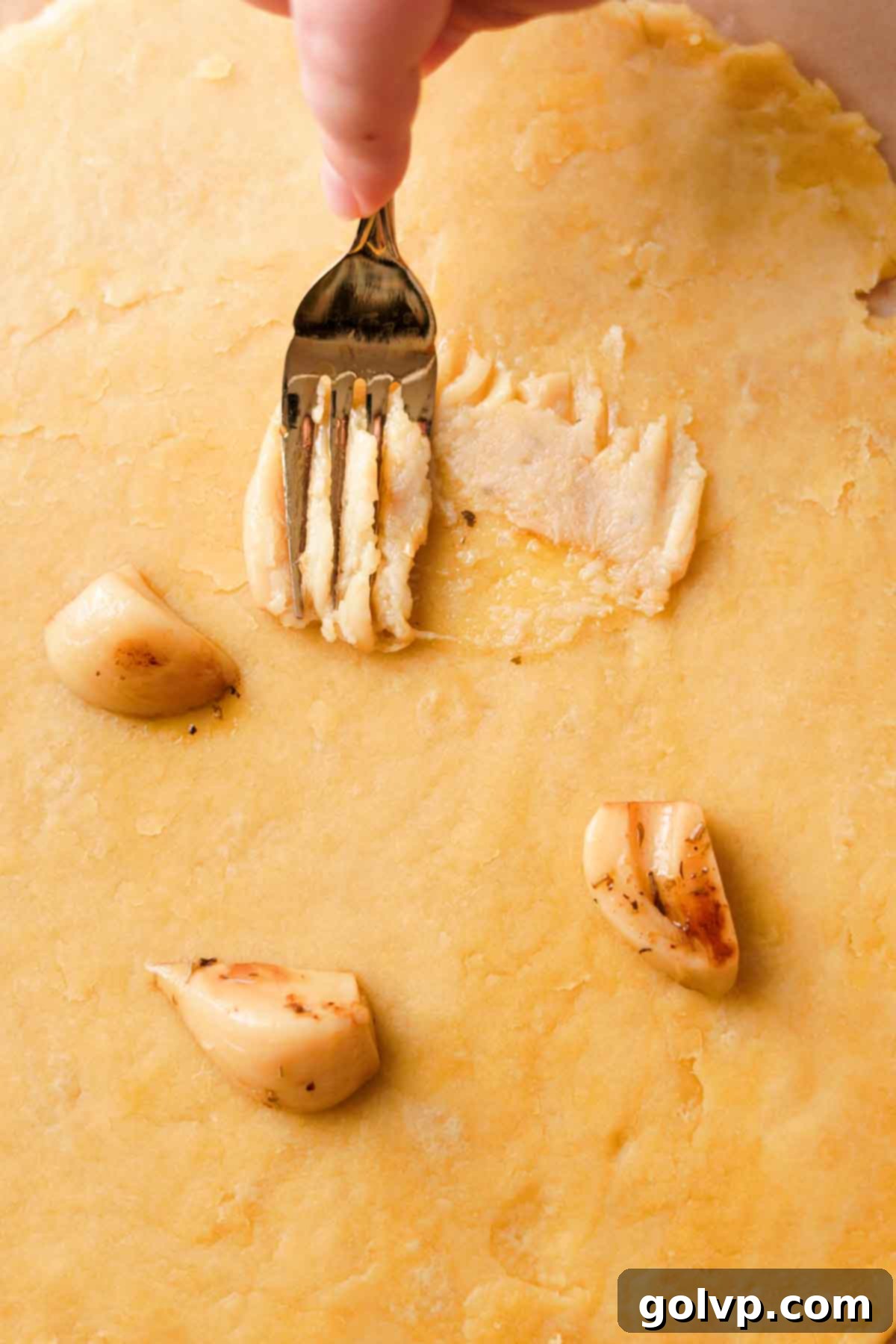 Mashing tender confit garlic with a fork directly onto the rolled-out pastry