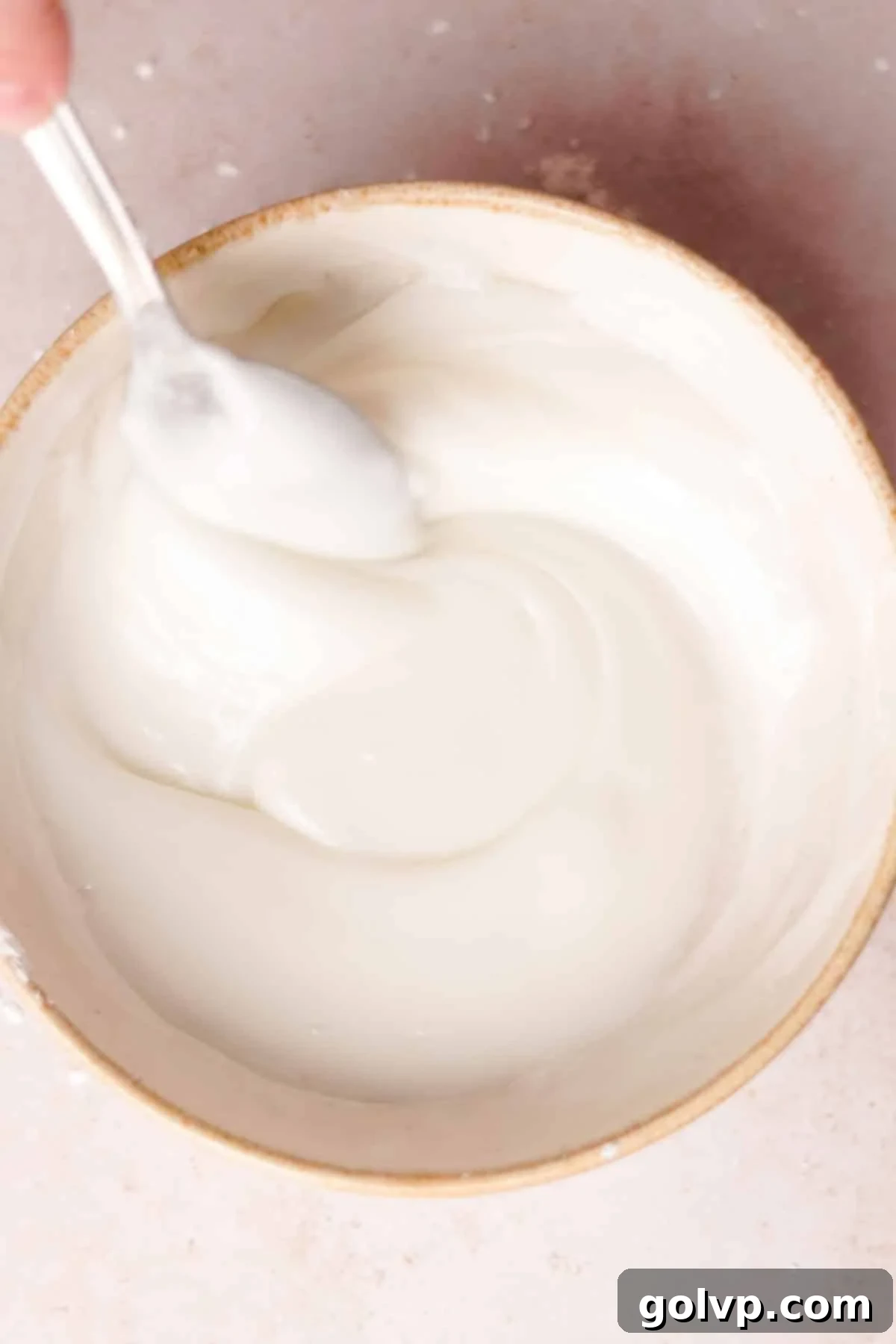 Stirring together powdered sugar and lemon juice to create a smooth, thick two-ingredient lemon glaze for cookies.