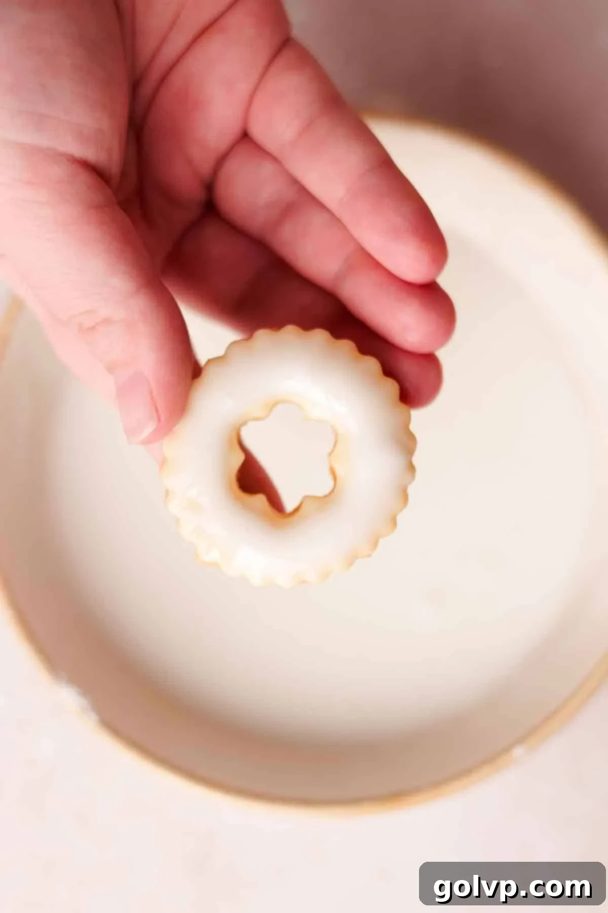 Dipping the tops of cooled lemon shortbread cookies into a vibrant lemon glaze, allowing excess to drip off.