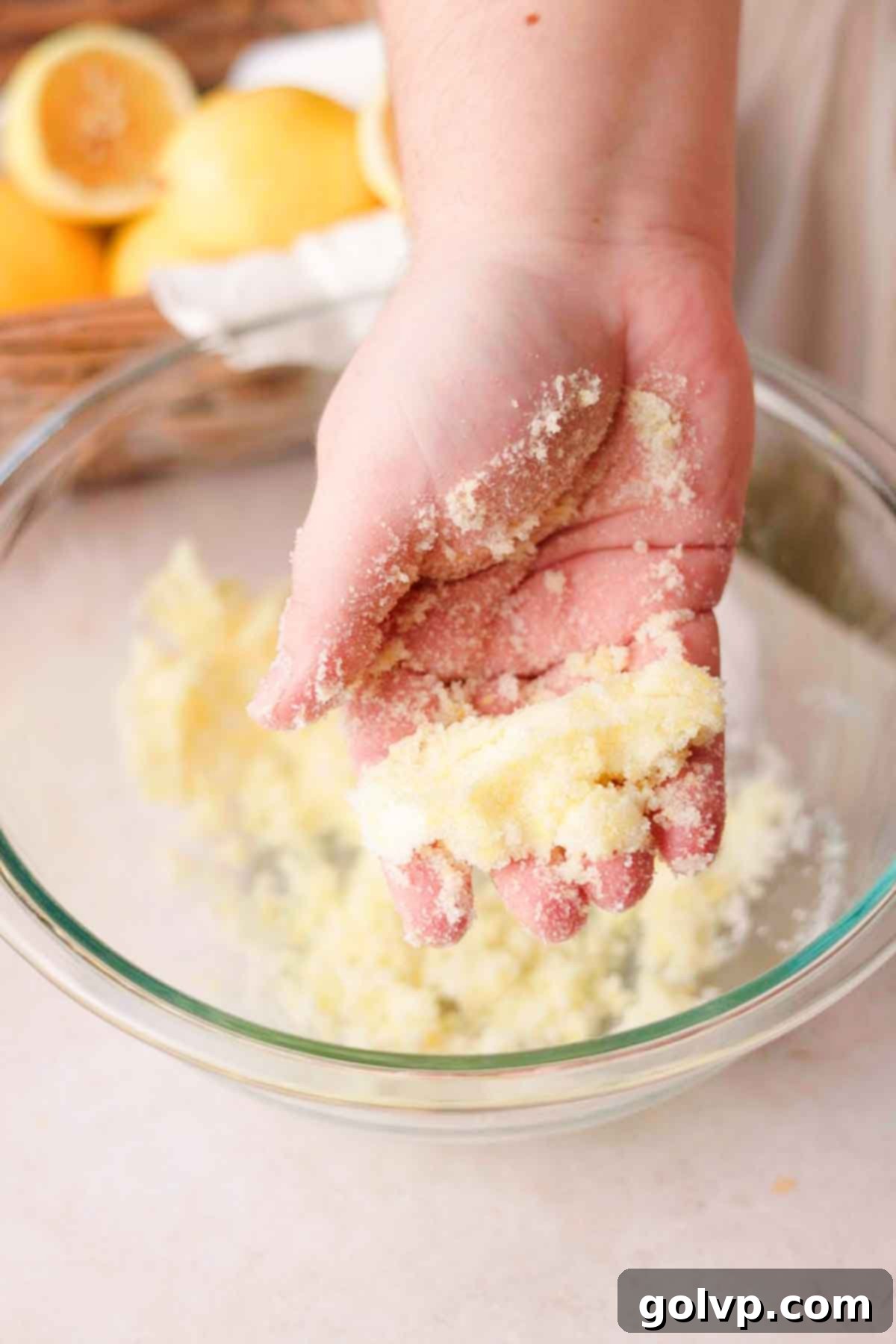 Rubbing granulated sugar and fresh lemon zest together with fingers in a bowl, creating a moist, fragrant yellow mixture.