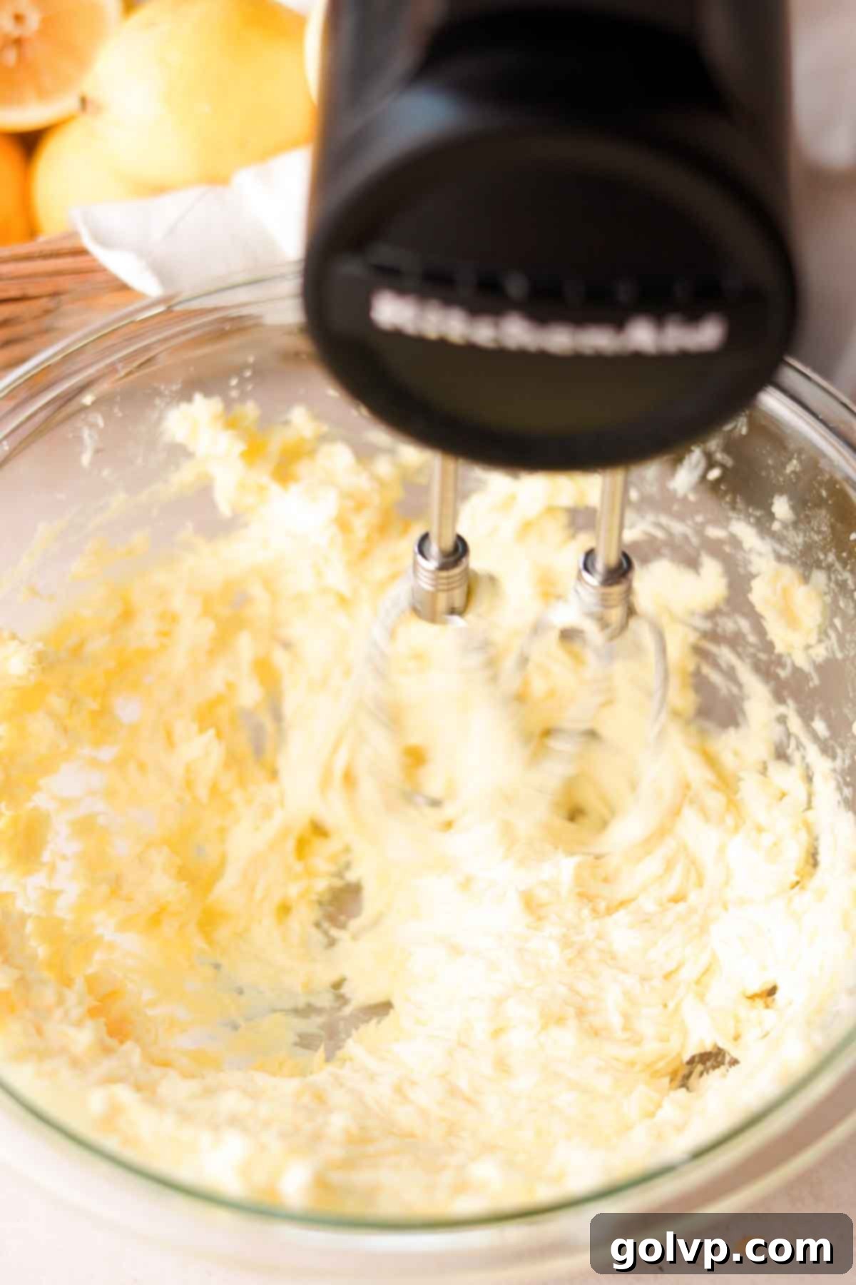 Mixing lemon juice and a large egg yolk into the creamed butter and sugar mixture with a handheld electric mixer.