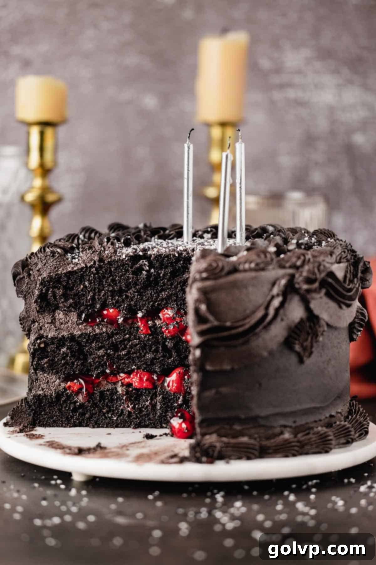 A beautifully sliced black velvet cake showing its rich black layers, contrasting black frosting, and a vibrant red cherry filling.