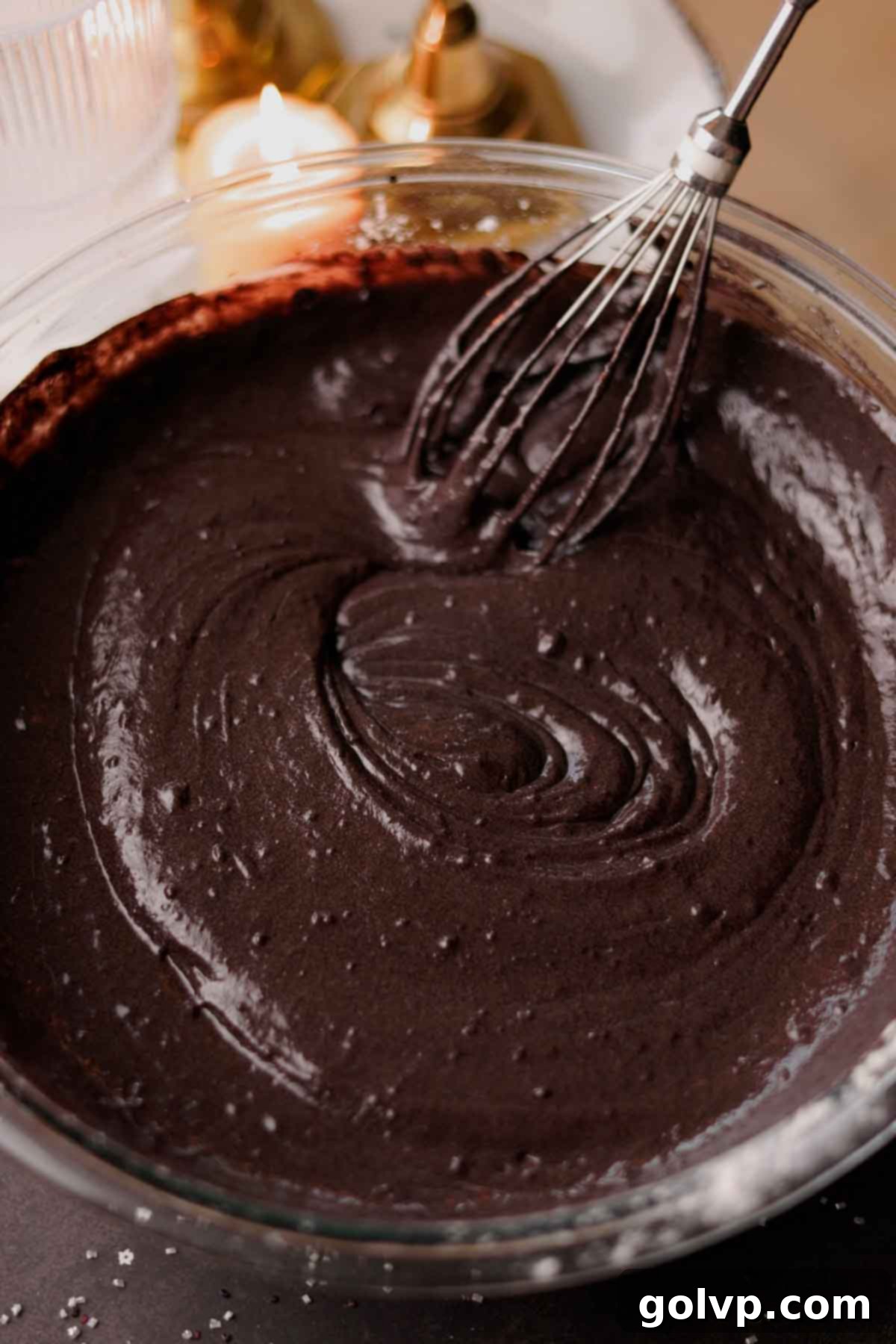 The black velvet cake batter being gently folded with a whisk after adding the bloomed cocoa mixture.