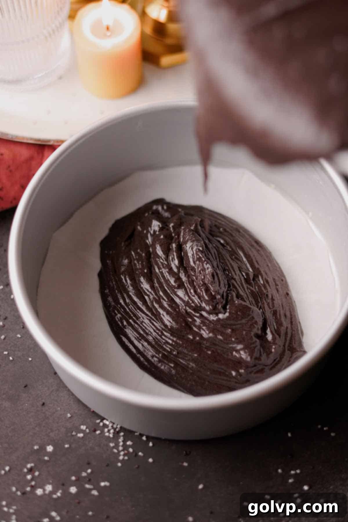 Cake pans being filled evenly with the dark black velvet cake batter.