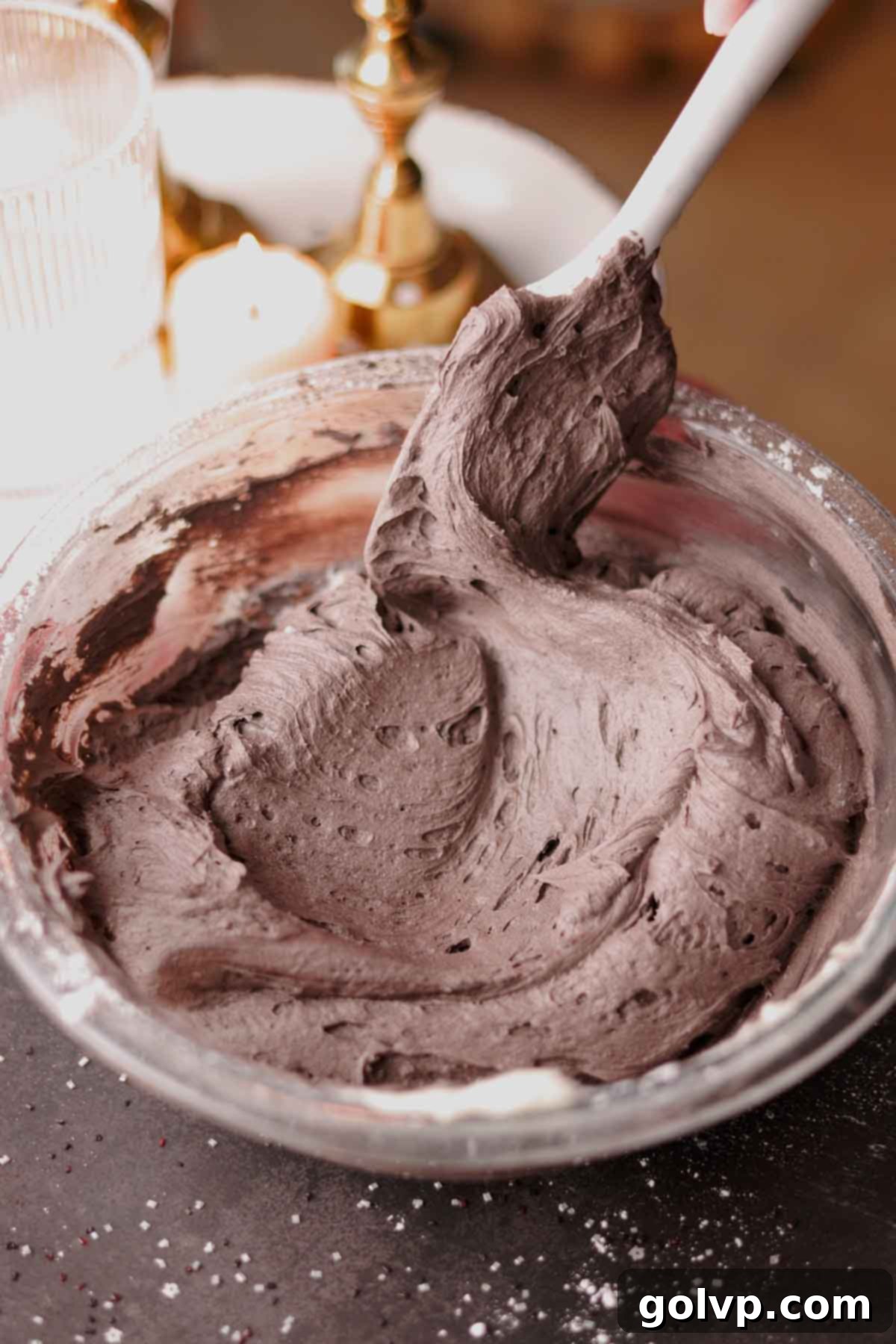 Black cocoa frosting being folded with a spatula, showing its rich, dark color and smooth texture.