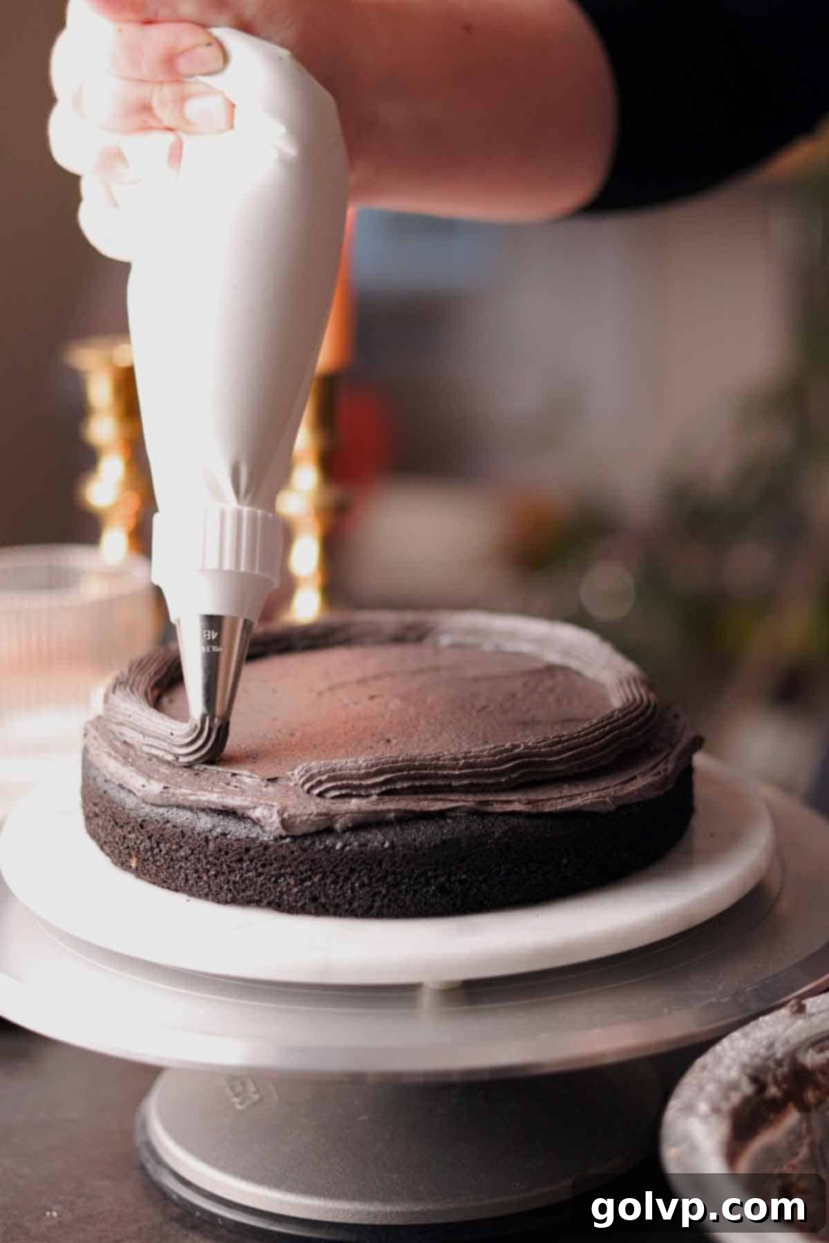 A border of black frosting being piped around the perimeter of a round cake layer.