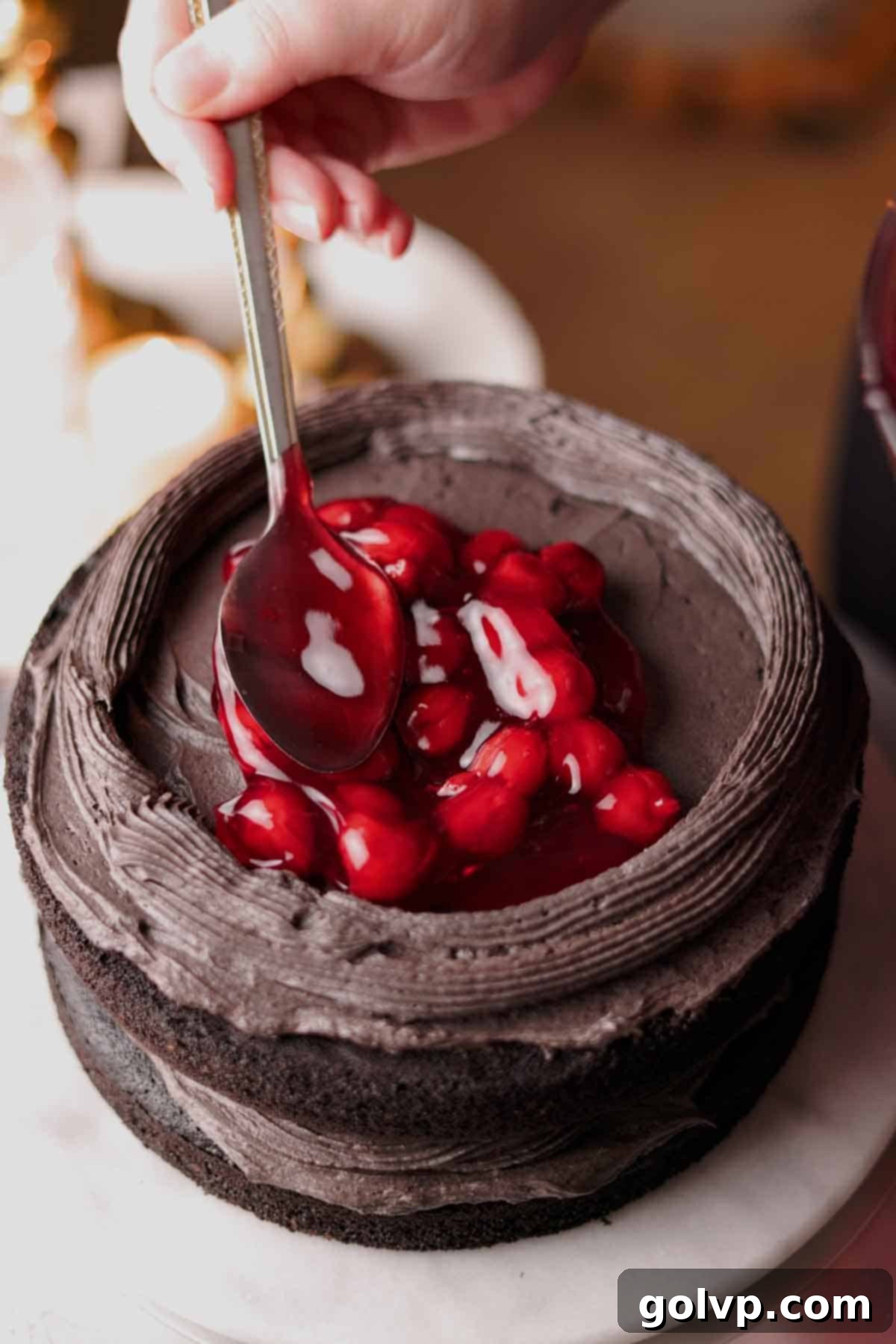 Filling the stacked cake layers with a generous amount of vibrant red cherry filling.