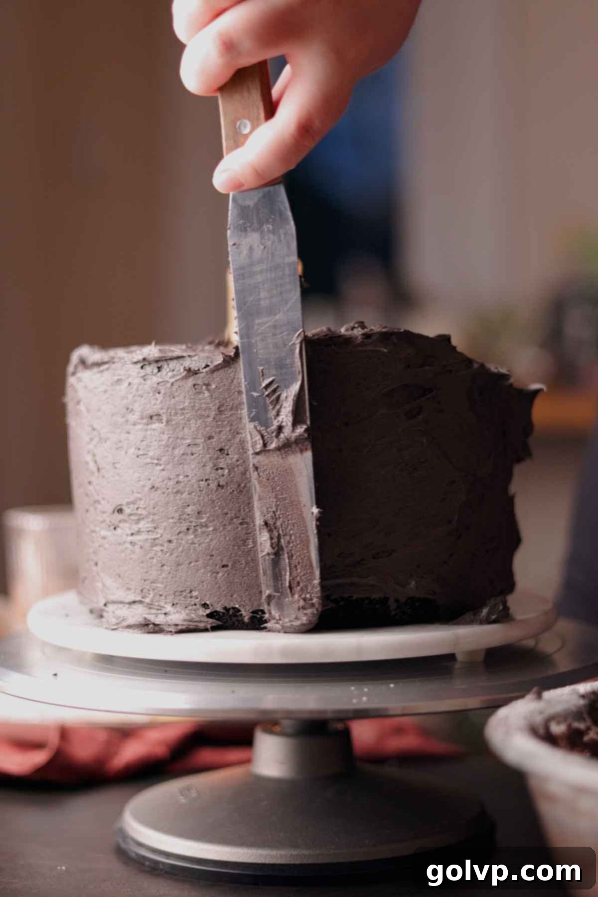Spreading a thin crumb coat of black cocoa frosting on the sides of a stacked cake.