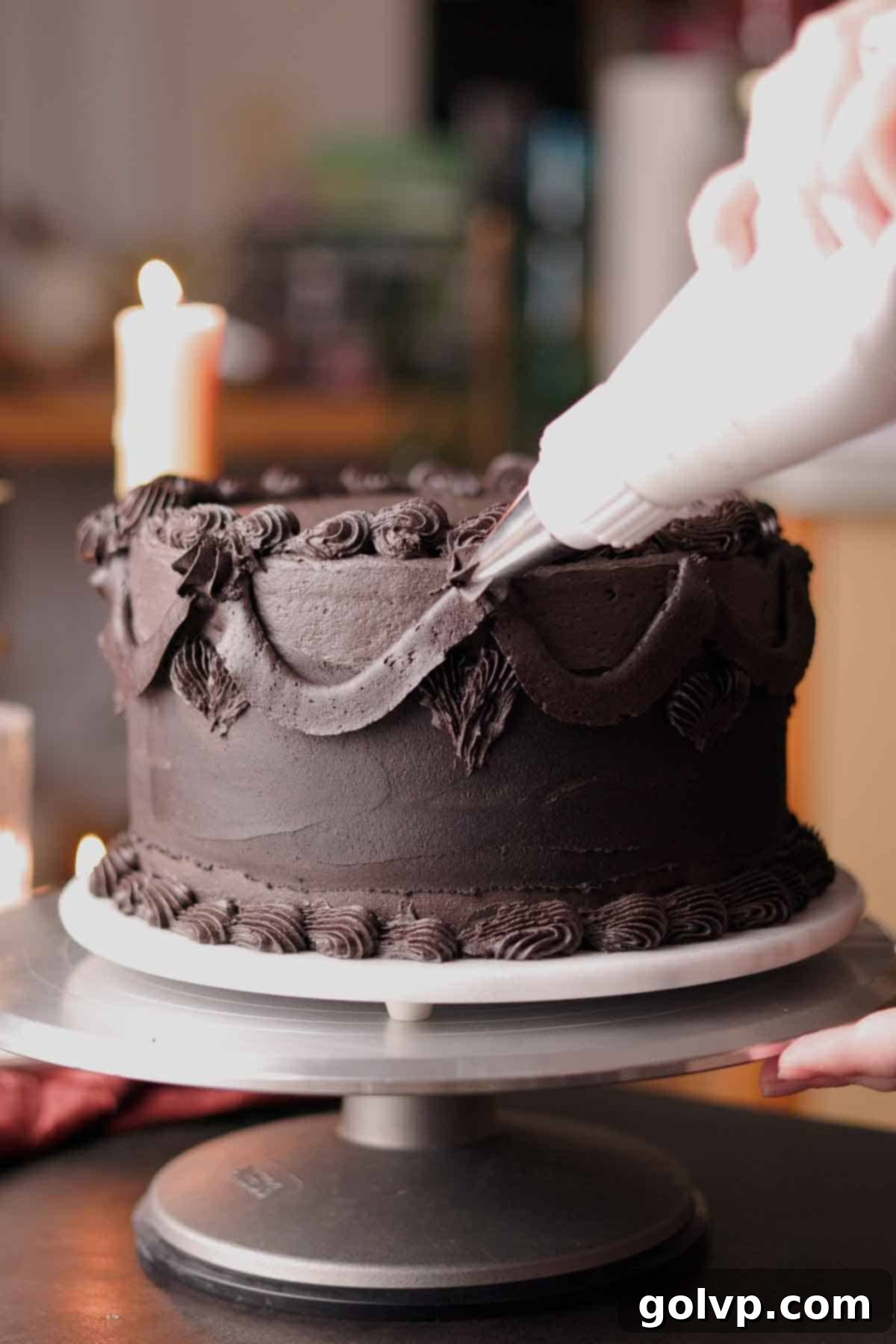 Decorating the black cake with elegant ruffles and swoops of black frosting using piping tips.