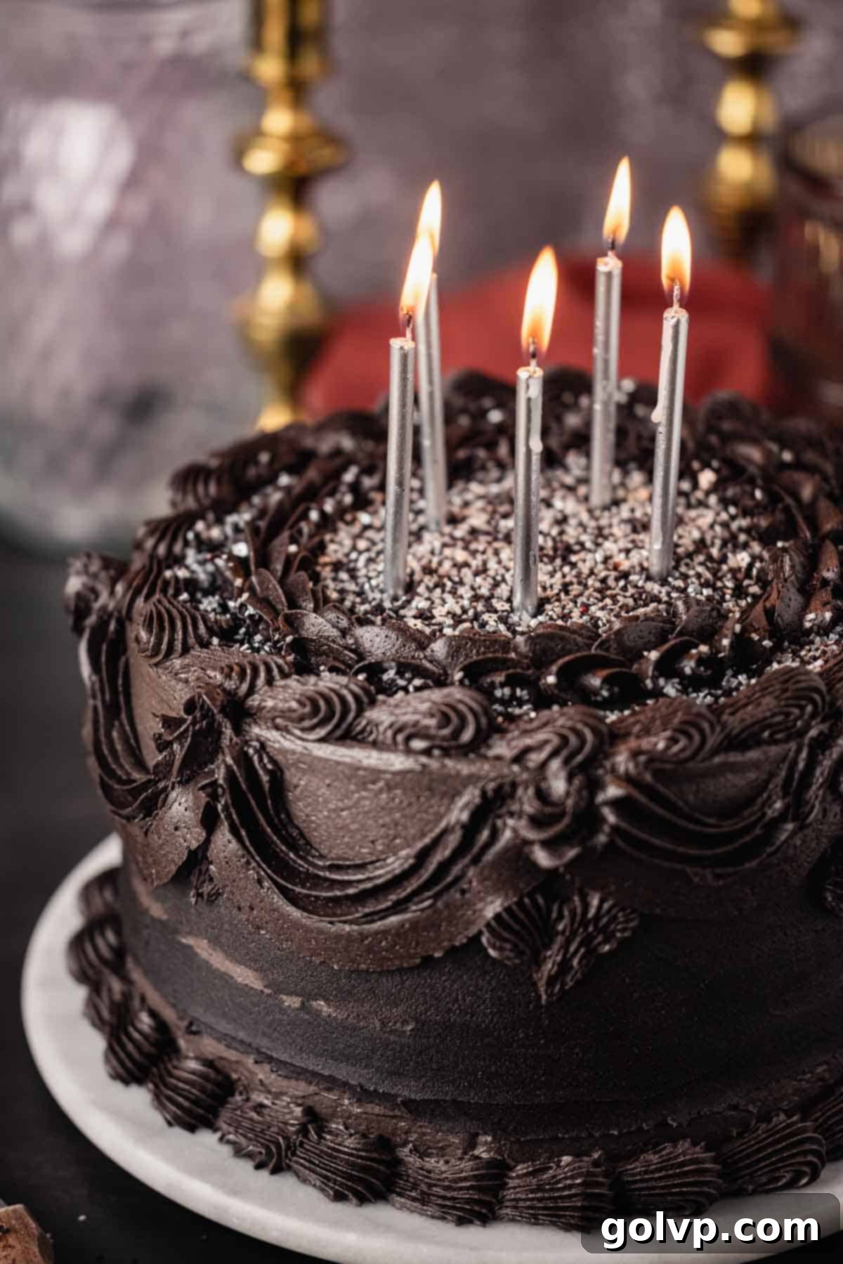 A stunning black velvet cake adorned with black frosting and sparkling lit silver candles, ready for celebration.