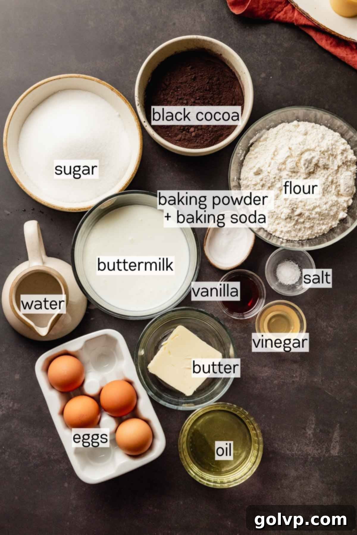 Bowls of perfectly measured ingredients for the black velvet cake layers, showcasing the black cocoa powder.