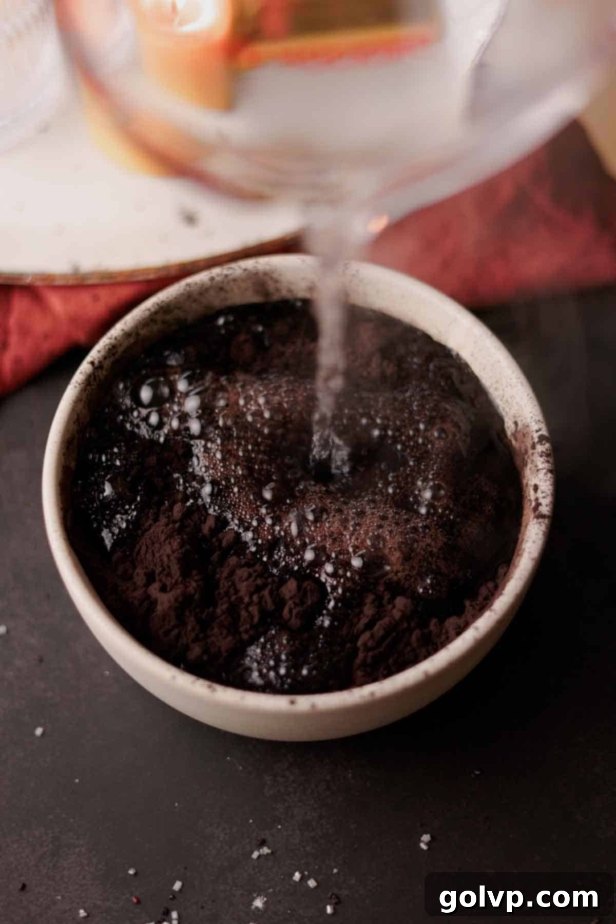 Hot water being poured over black cocoa powder in a bowl, creating a rich paste.