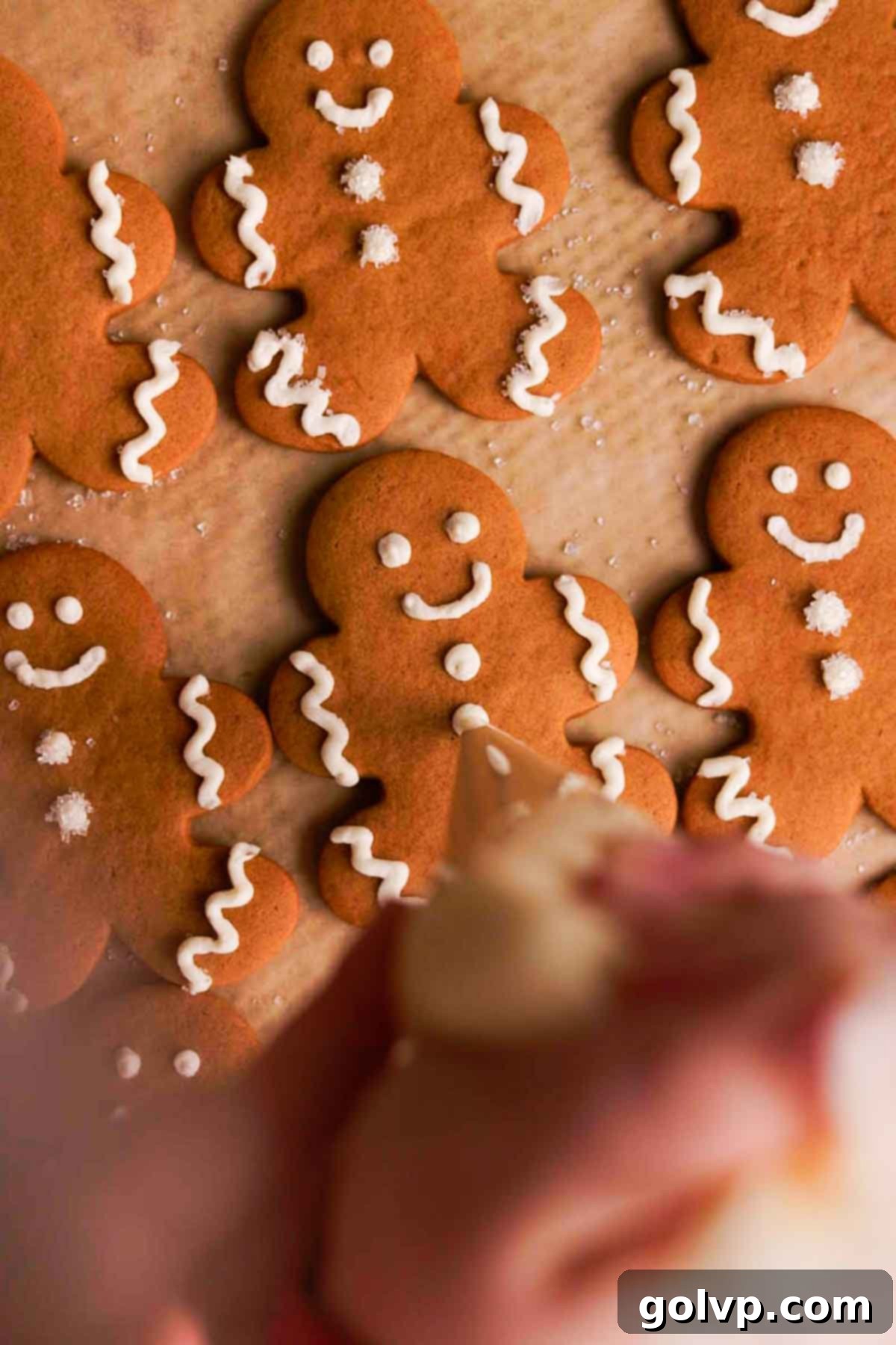 Decorating gingerbread men cookies by piping small white buttons with a plastic piping bag