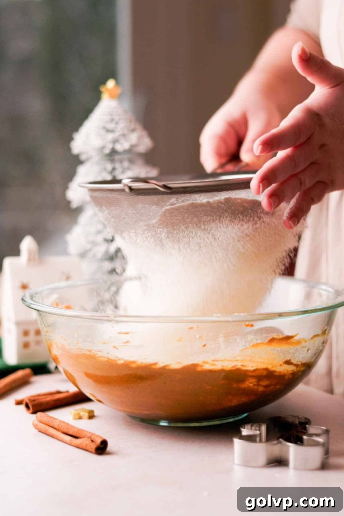 Sifting all-purpose flour into a bowl using a metal sieve for gingerbread cookie dough