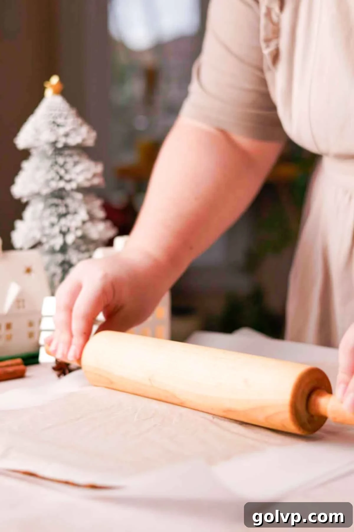 Rolling out gingerbread dough evenly between two sheets of parchment paper with a wooden rolling pin