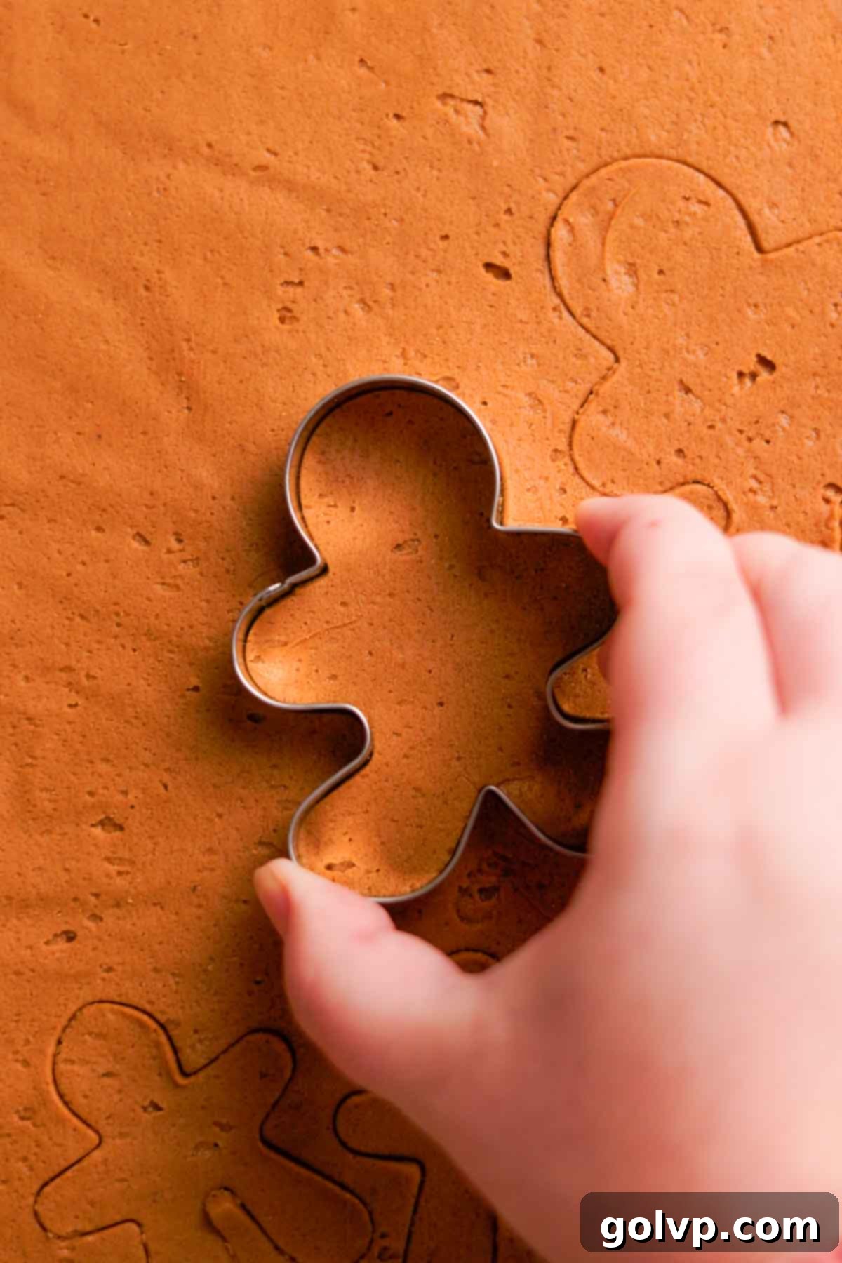 Cutting out gingerbread men shapes from chilled dough using festive cookie cutters