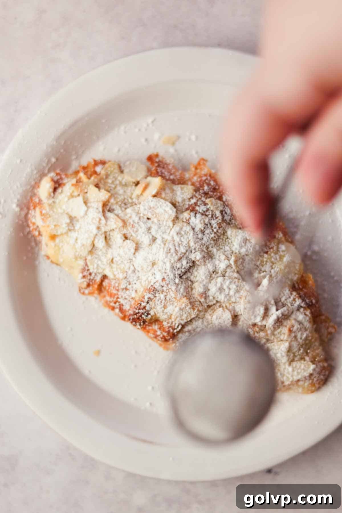 sprinkling croissant on a plate with powdered sugar