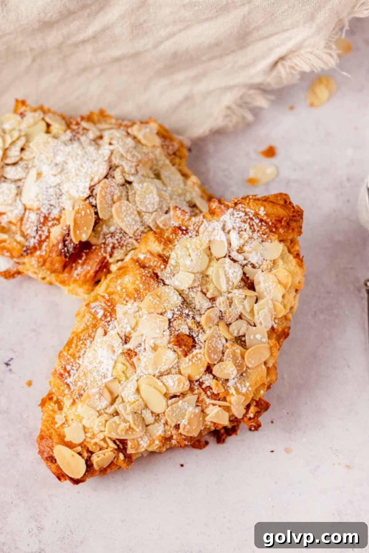 almond croissant on counter topped with sliced almonds and dusted with powdered sugar