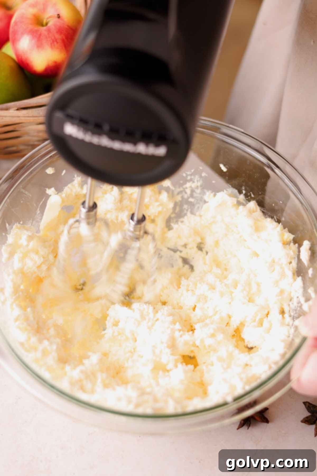 beating butter and cream cheese in a large glass bowl with an electric mixer