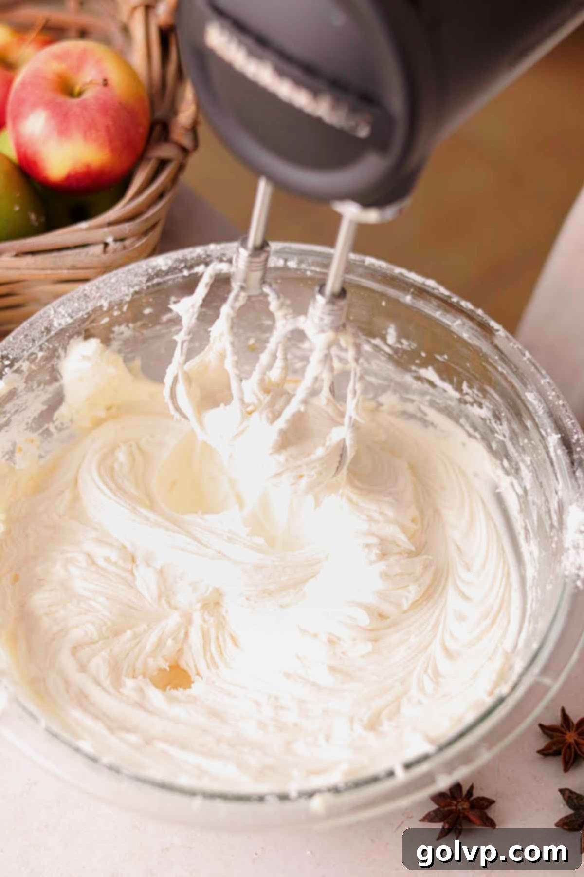 beating cream cheese frosting with electric mixer in glass bowl