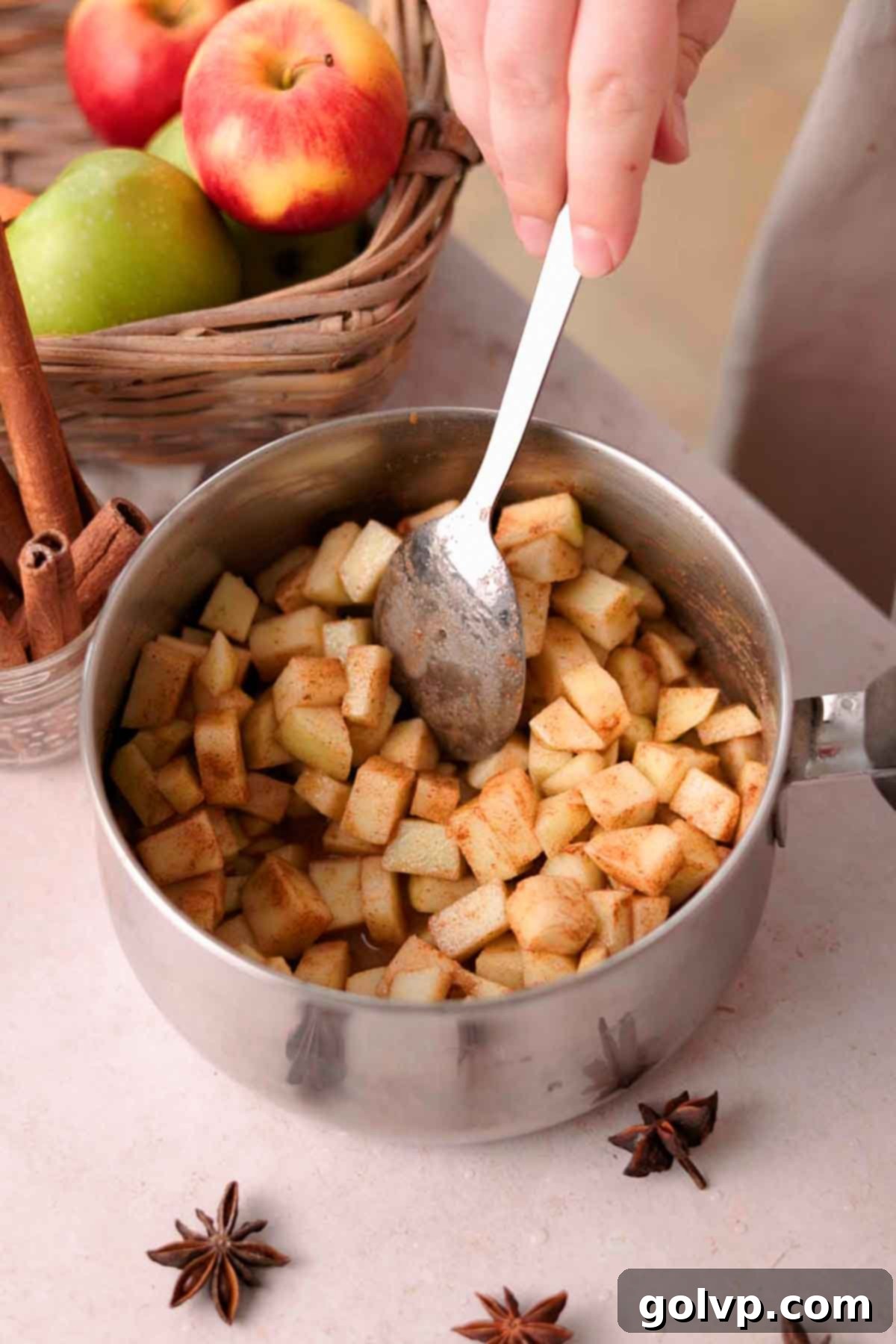 using spoon to stir cubed apples and spices in small pot