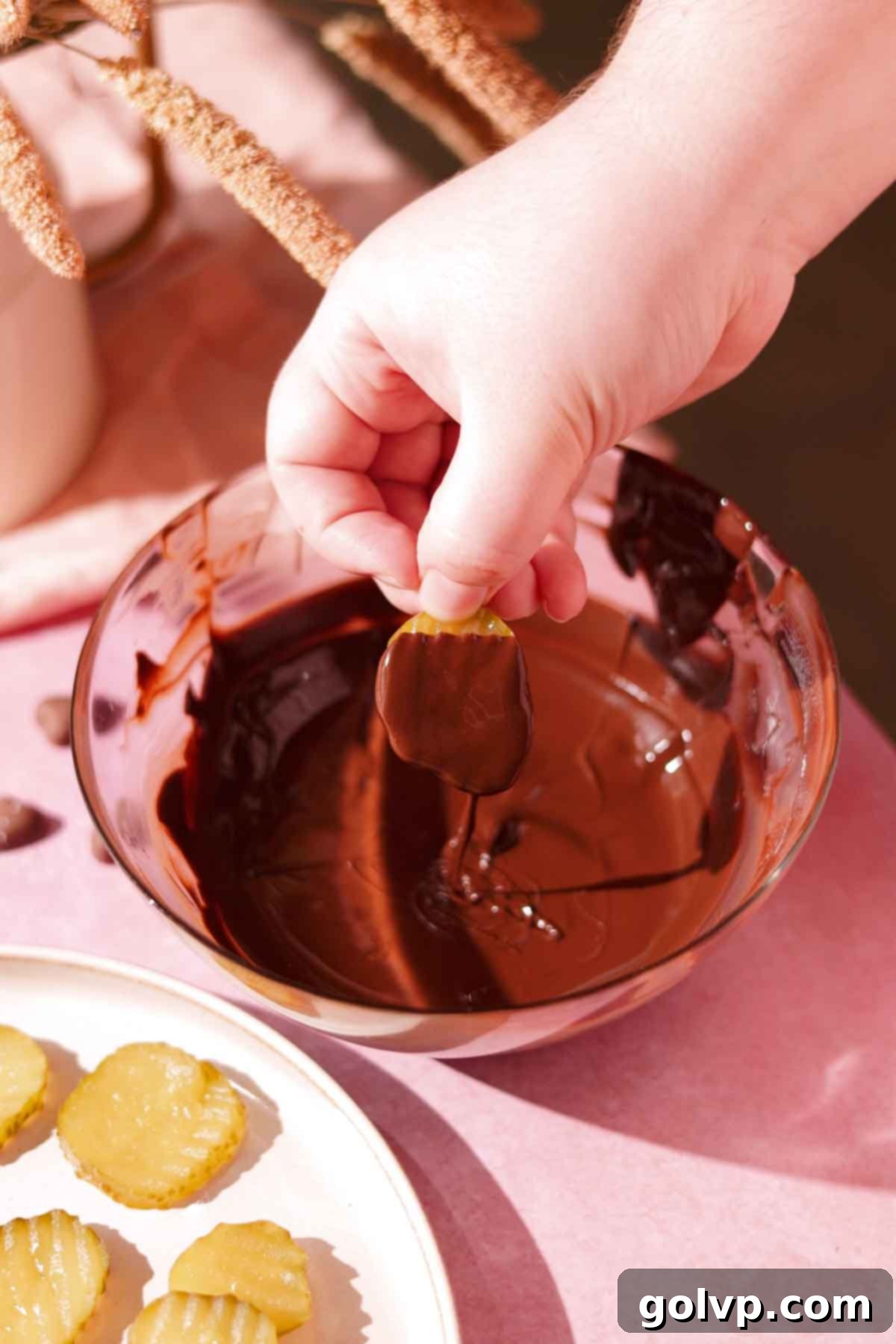 hand dipping pickle slices in glass bowl full of melted chocolate