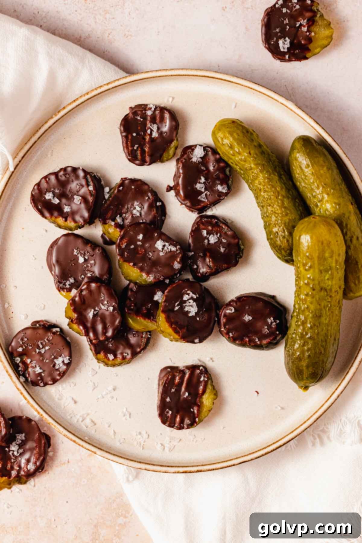 chocolate covered pickle slices with flaky salt on a plate with whole pickles on the side