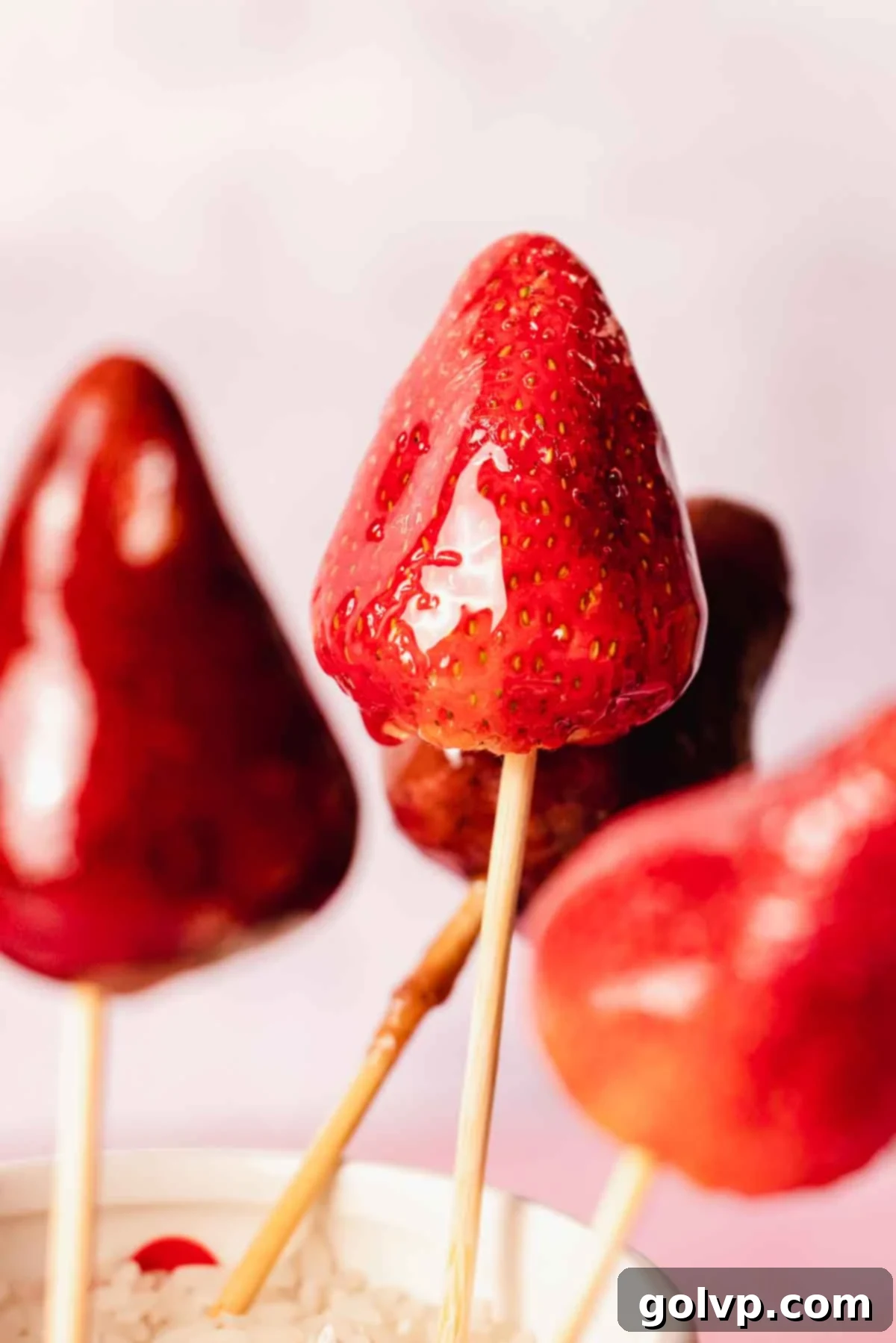 Shiny strawberry tanghulu standing up inside a clear glass cup, showcasing the crisp candy coating