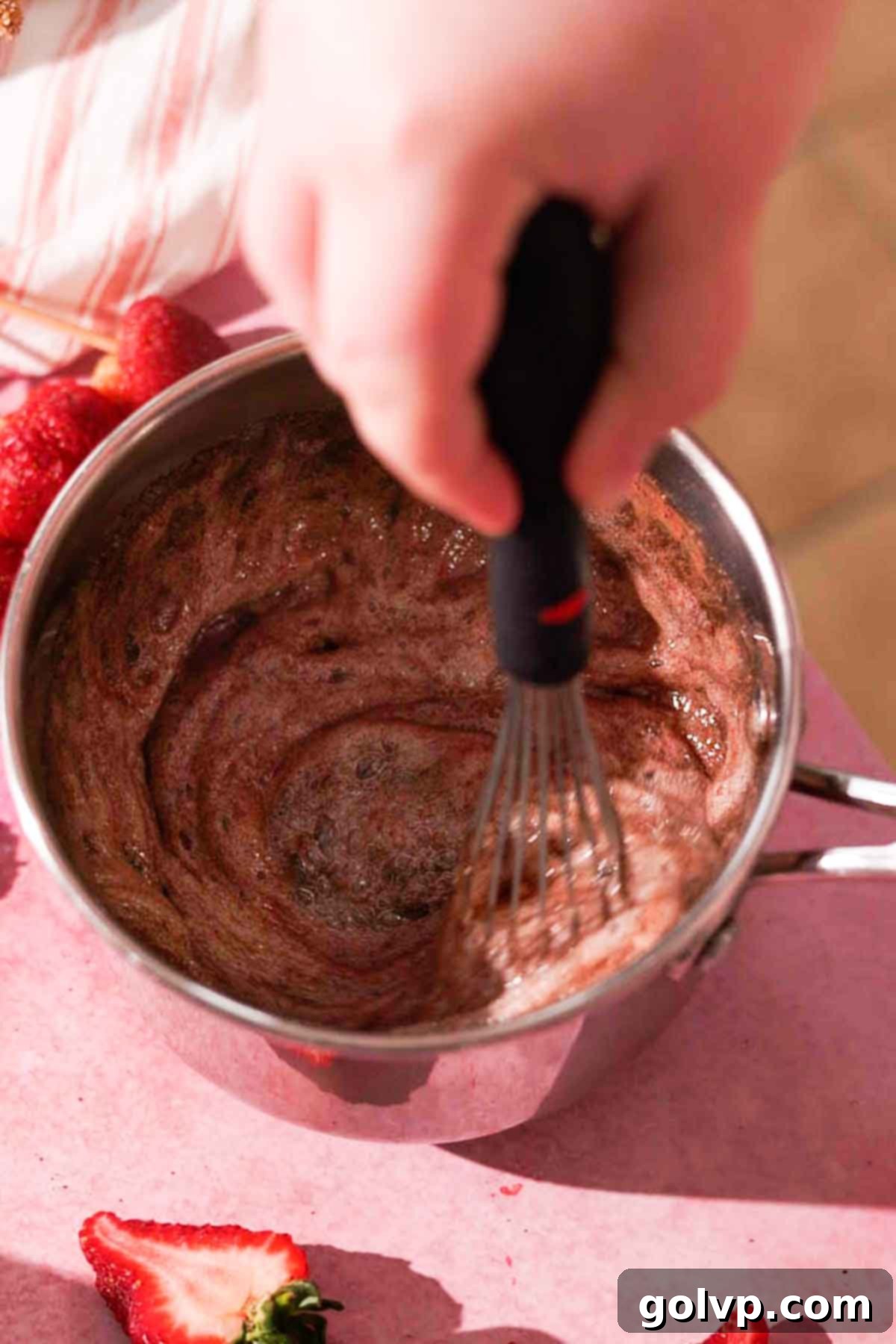 Whisking sifted cocoa powder into hot, foaming sugar syrup in a saucepan to create chocolate Tanghulu syrup