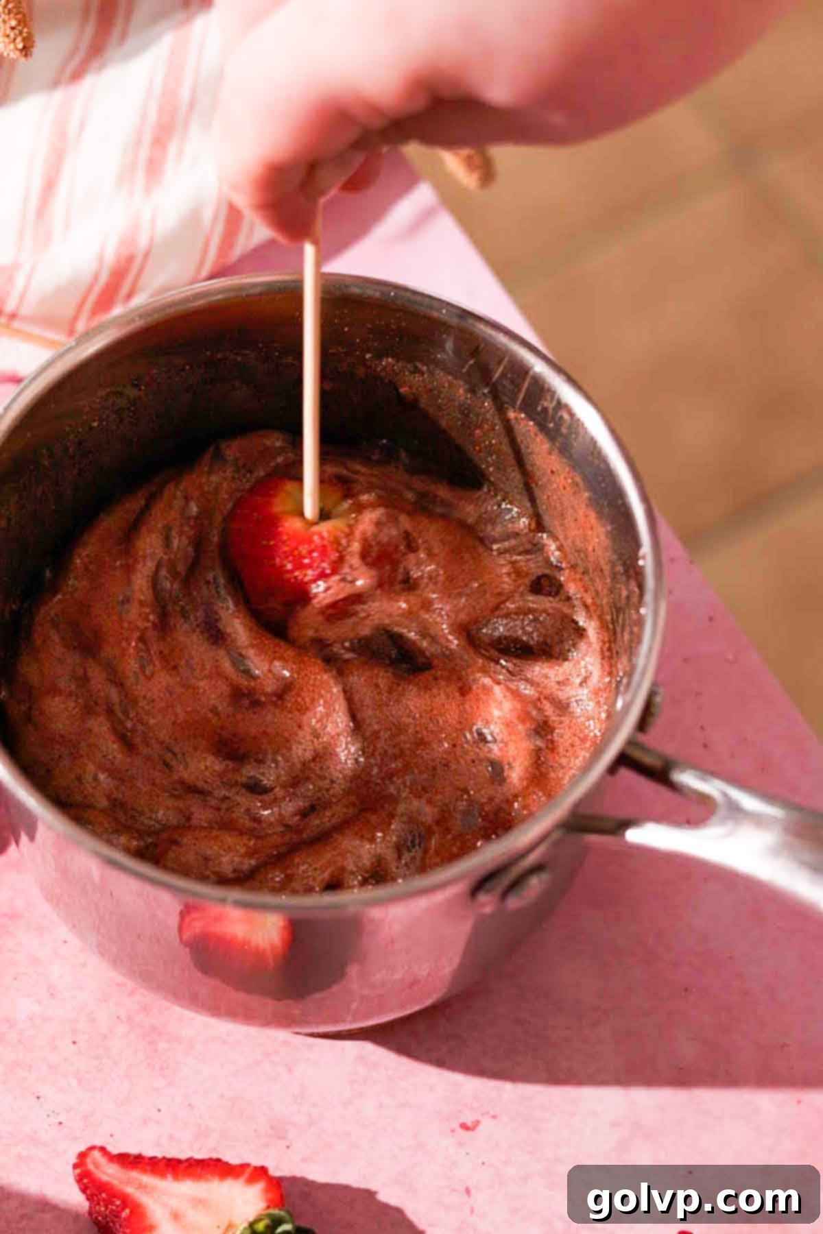 Dipping a strawberry on a skewer into the hot, dark, foaming chocolate sugar syrup