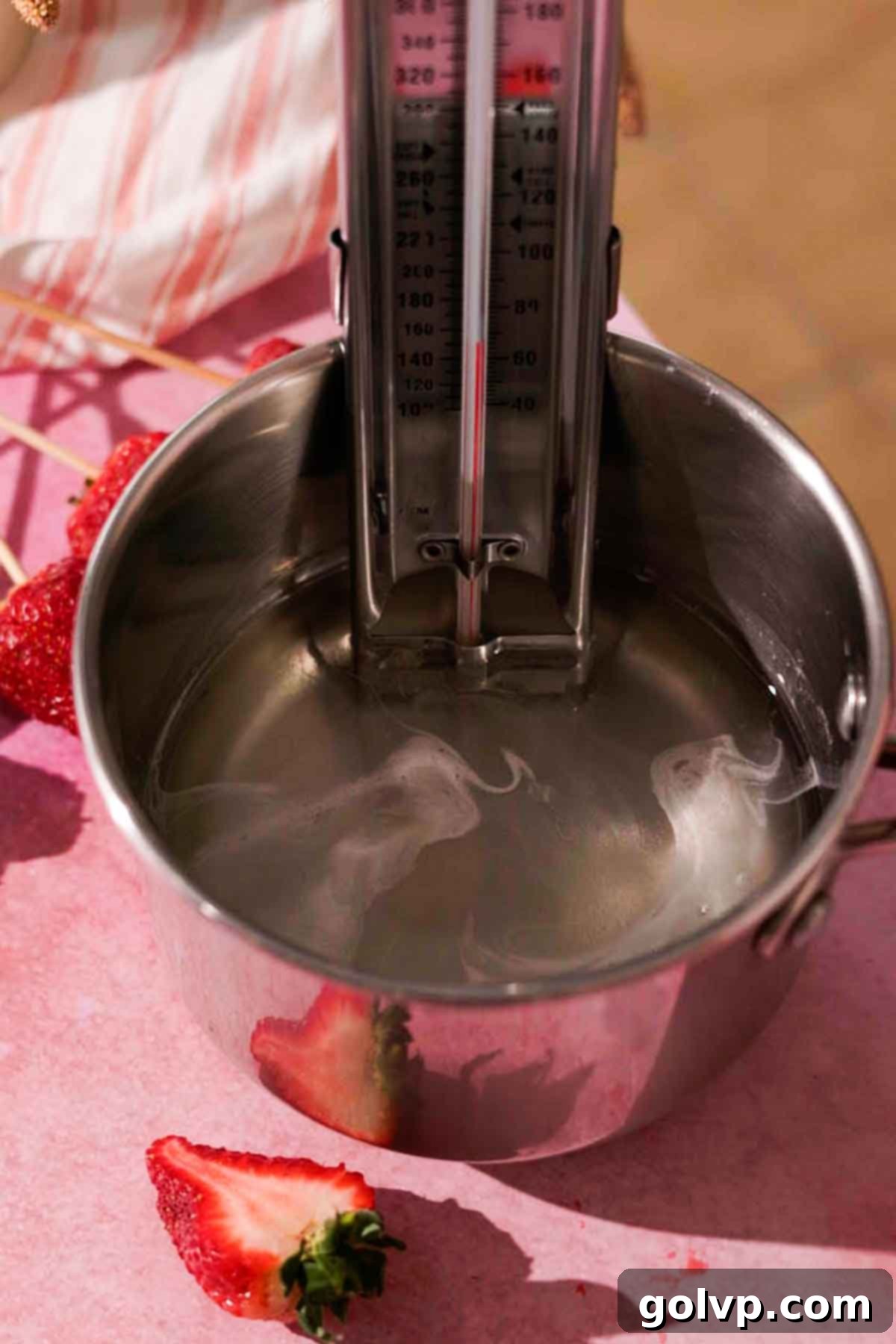 Small saucepan with a candy thermometer immersed in bubbling sugar syrup on a stove