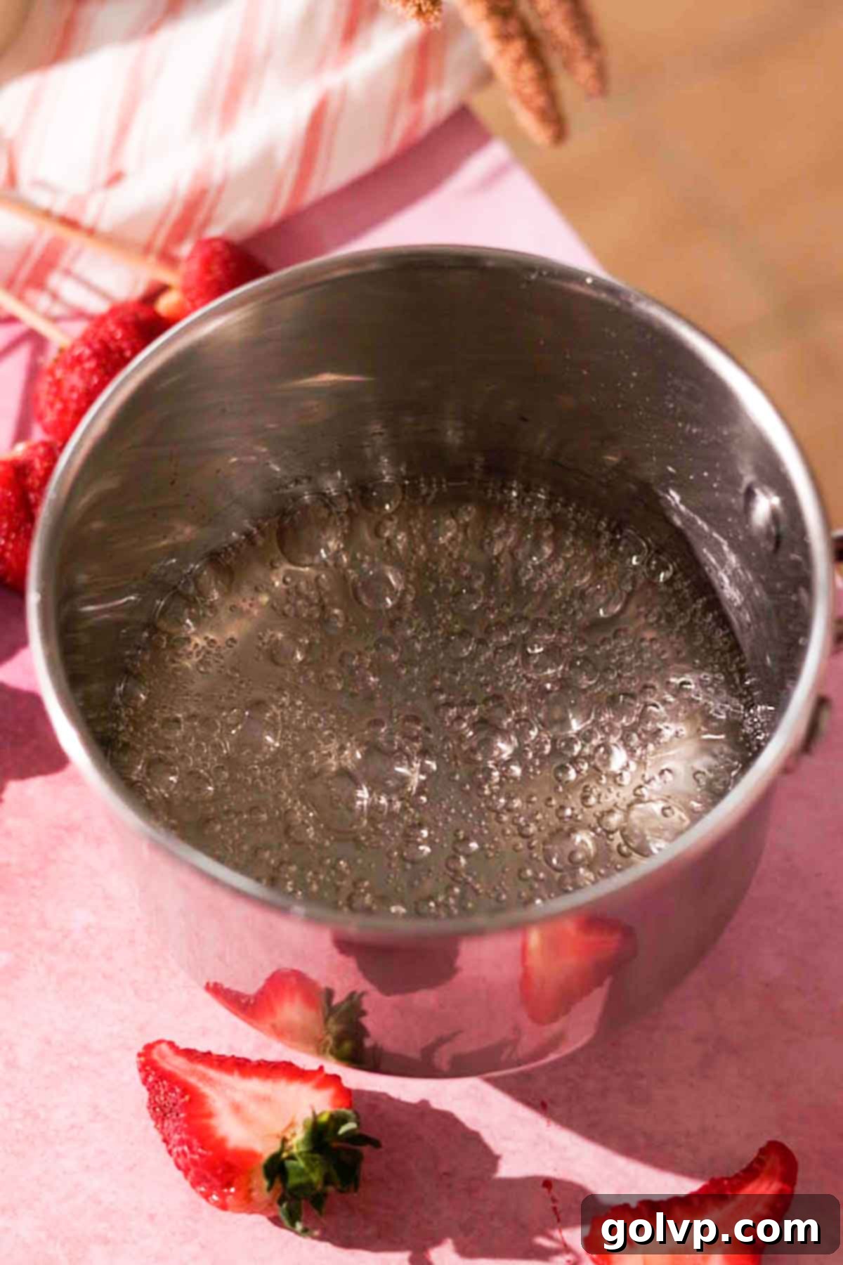 Simmering sugar syrup in a small saucepan, showing minimal golden color as it reaches the desired temperature