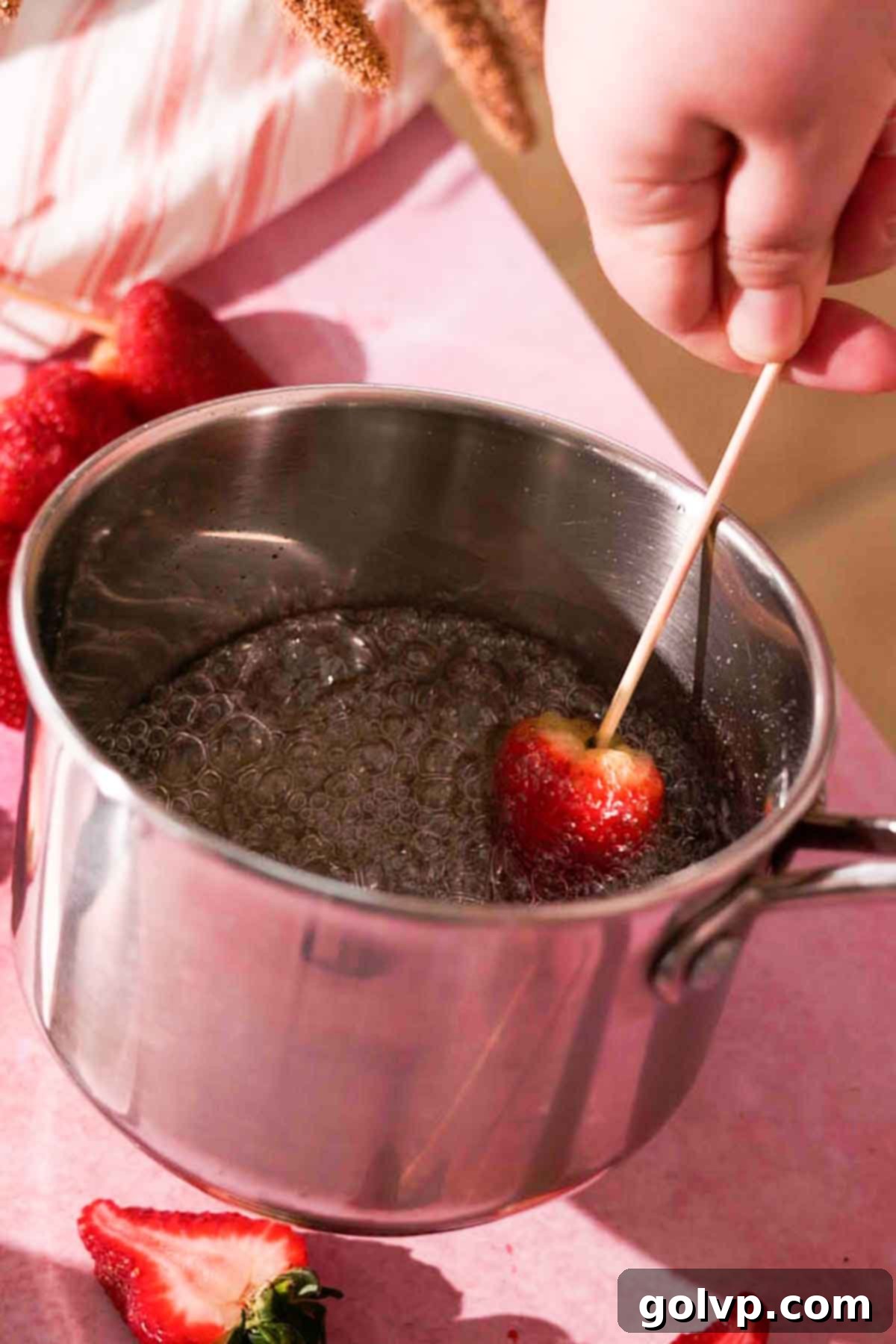 Dipping a strawberry on a skewer into the hot, foamy sugar syrup for a perfect coating