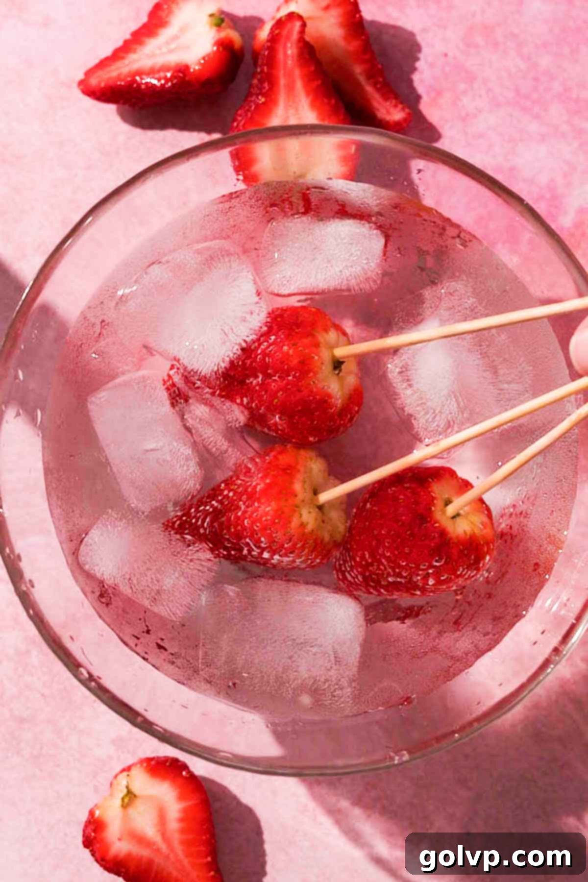 Dipping a freshly coated strawberry Tanghulu into a bowl of ice water to quickly set the sugar