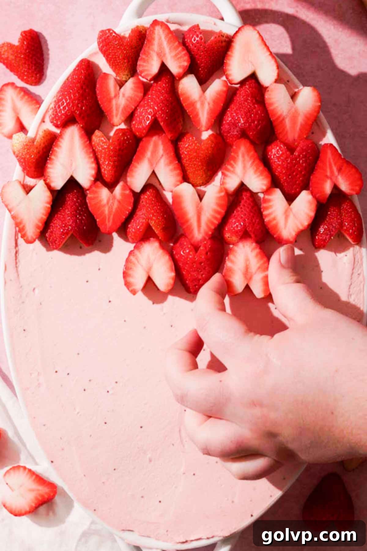arranging strawberry hearts onto top of strawberry tiramisu in alternating pattern