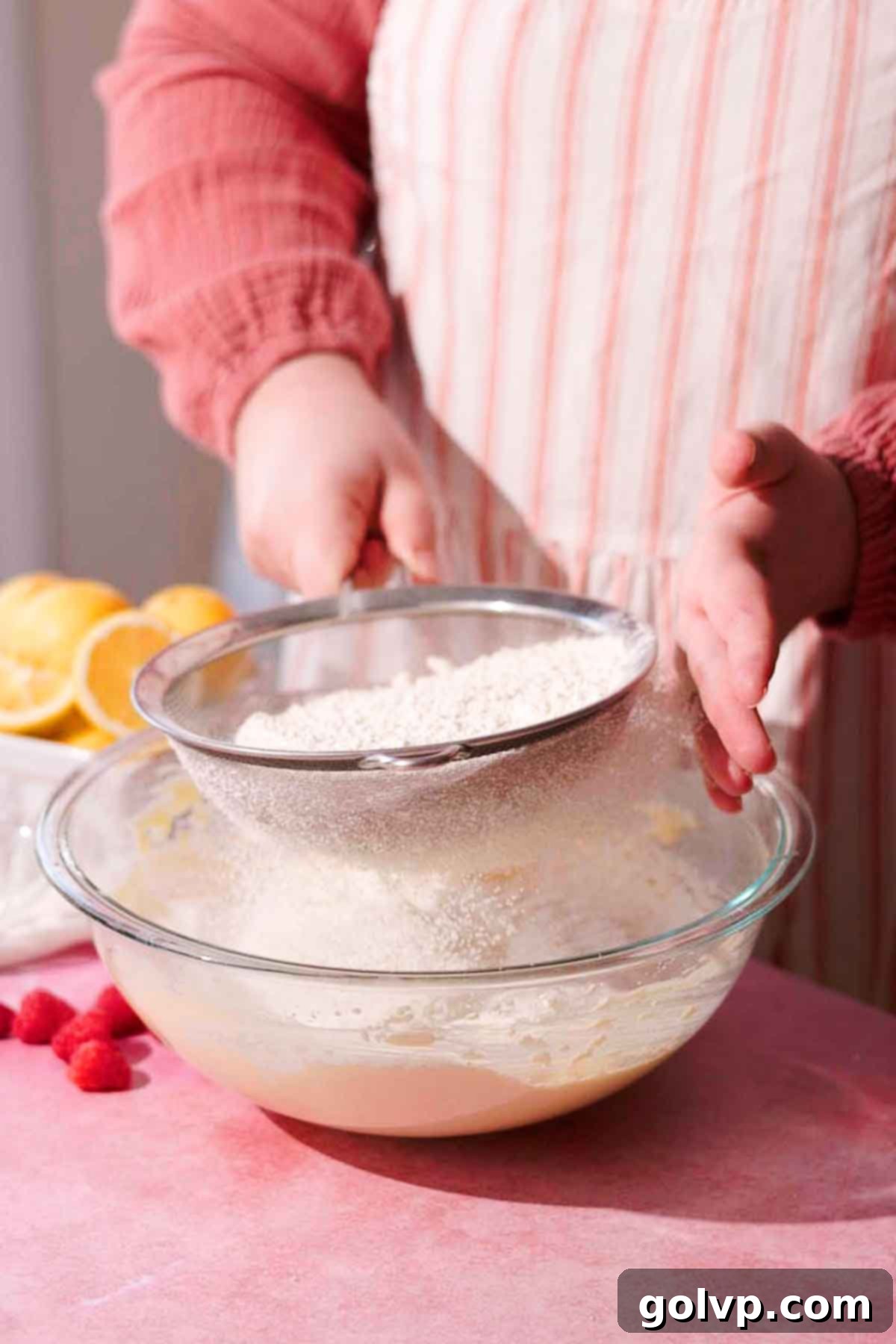 sifting flour with a metal sieve into a glass bowl of batter