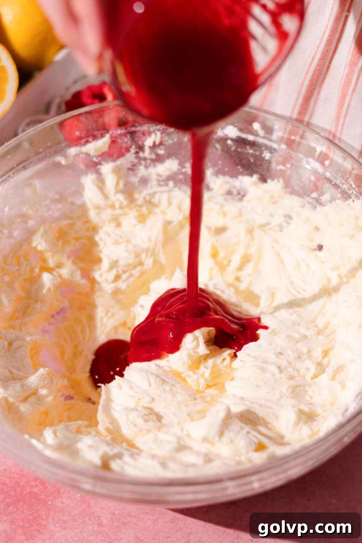 adding raspberry puree to frosting in large glass bowl