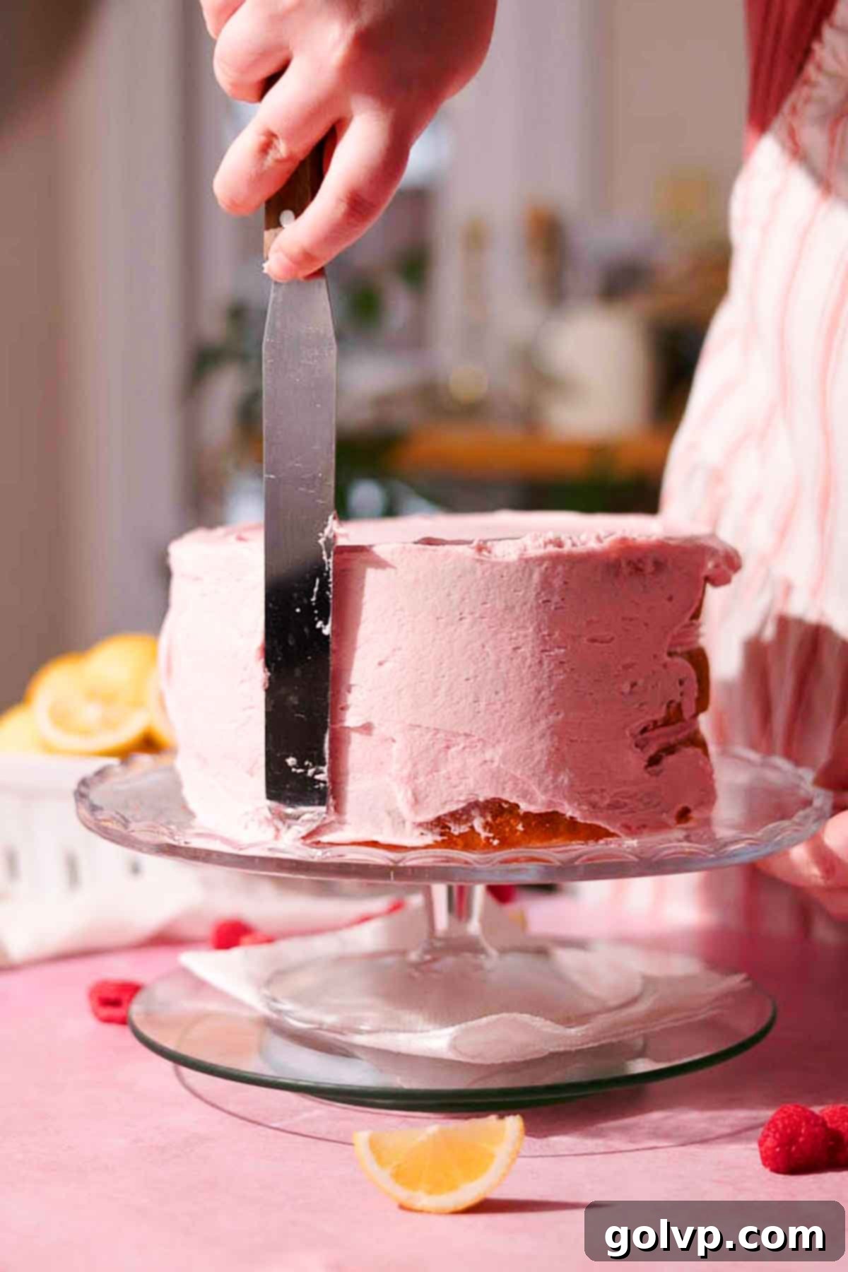 covering the sides of the cake with pink frosting using a long metal spatula 