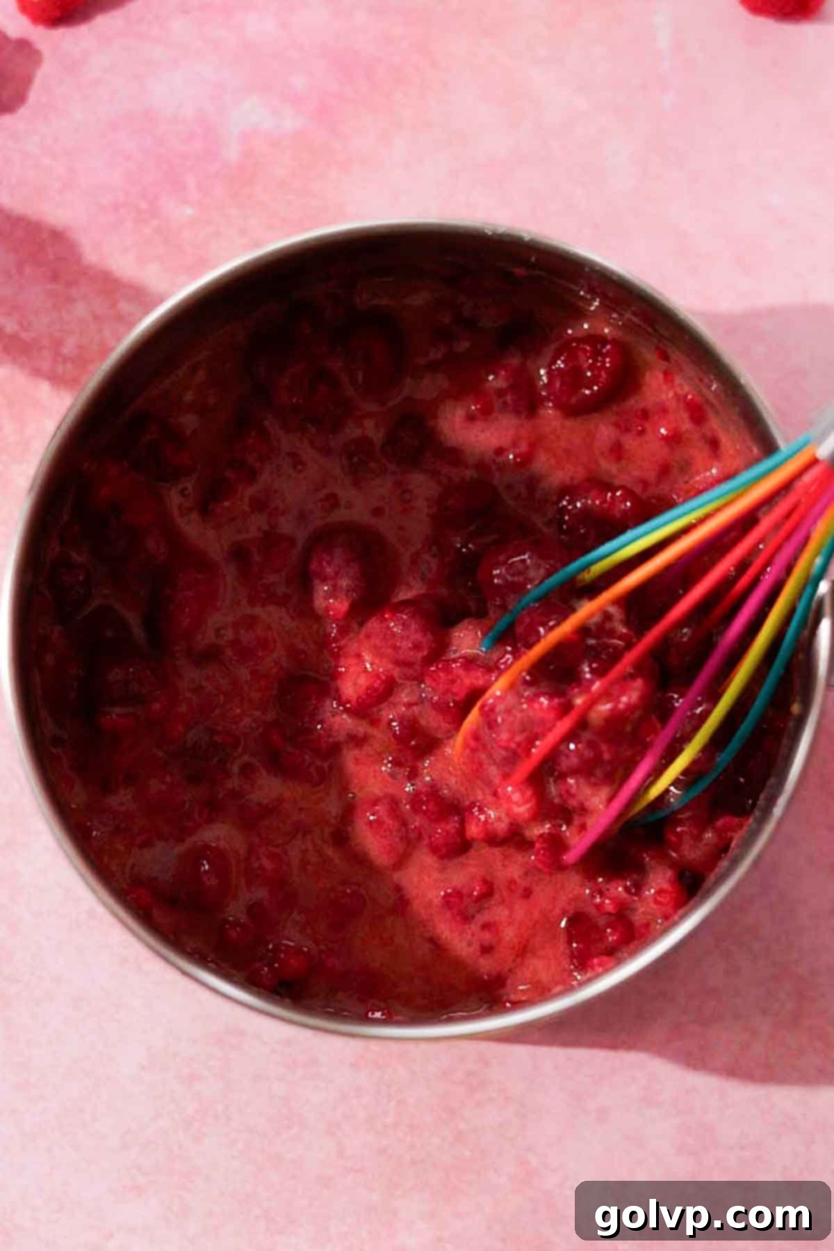 stirring uncooked raspberry curd with a silicone whisk in metal saucepan