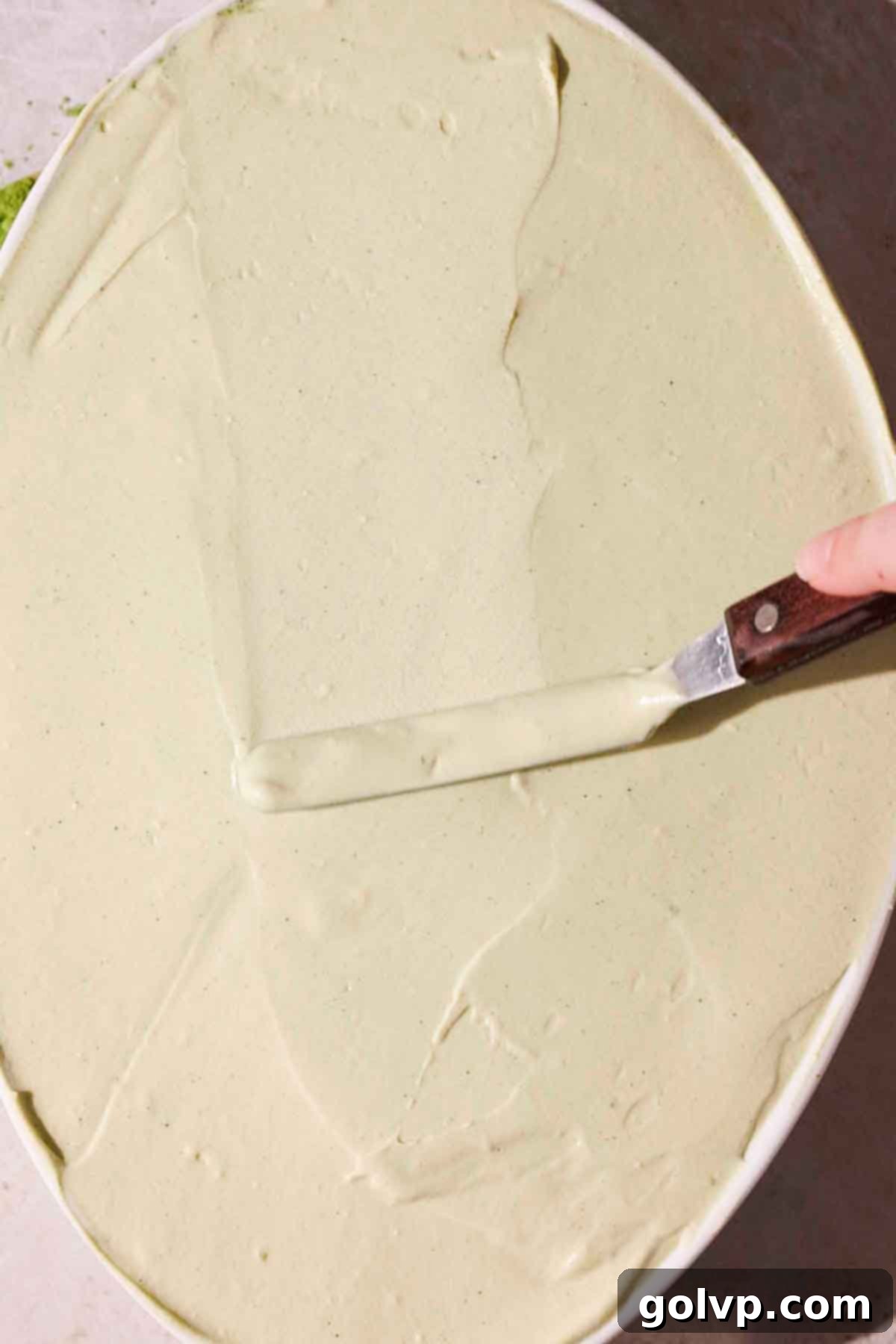 smoothing the top layer of matcha tiramisu filling with an offset spatula