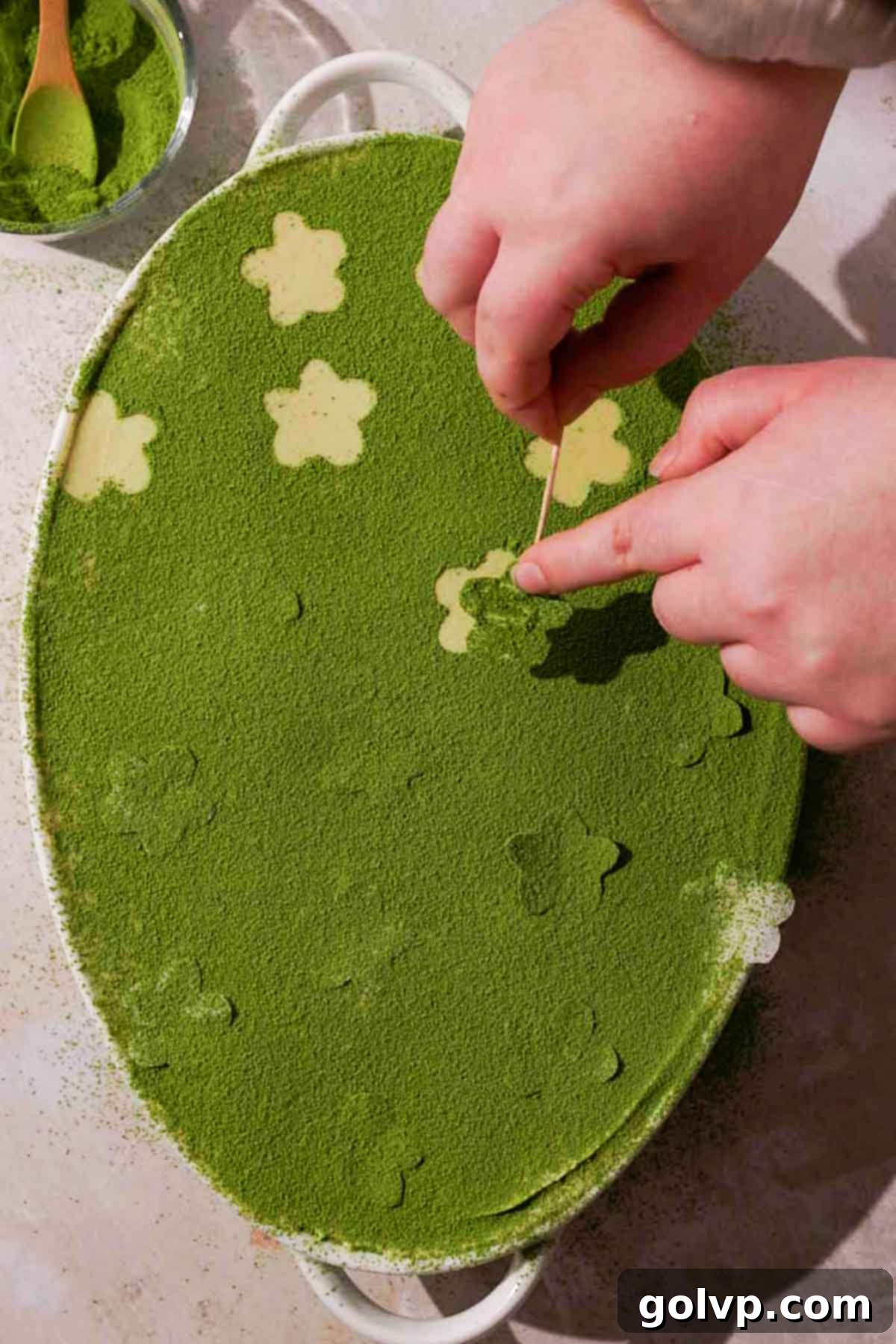removing parchment paper flower stencils from a matcha dusted tiramisu for decoration