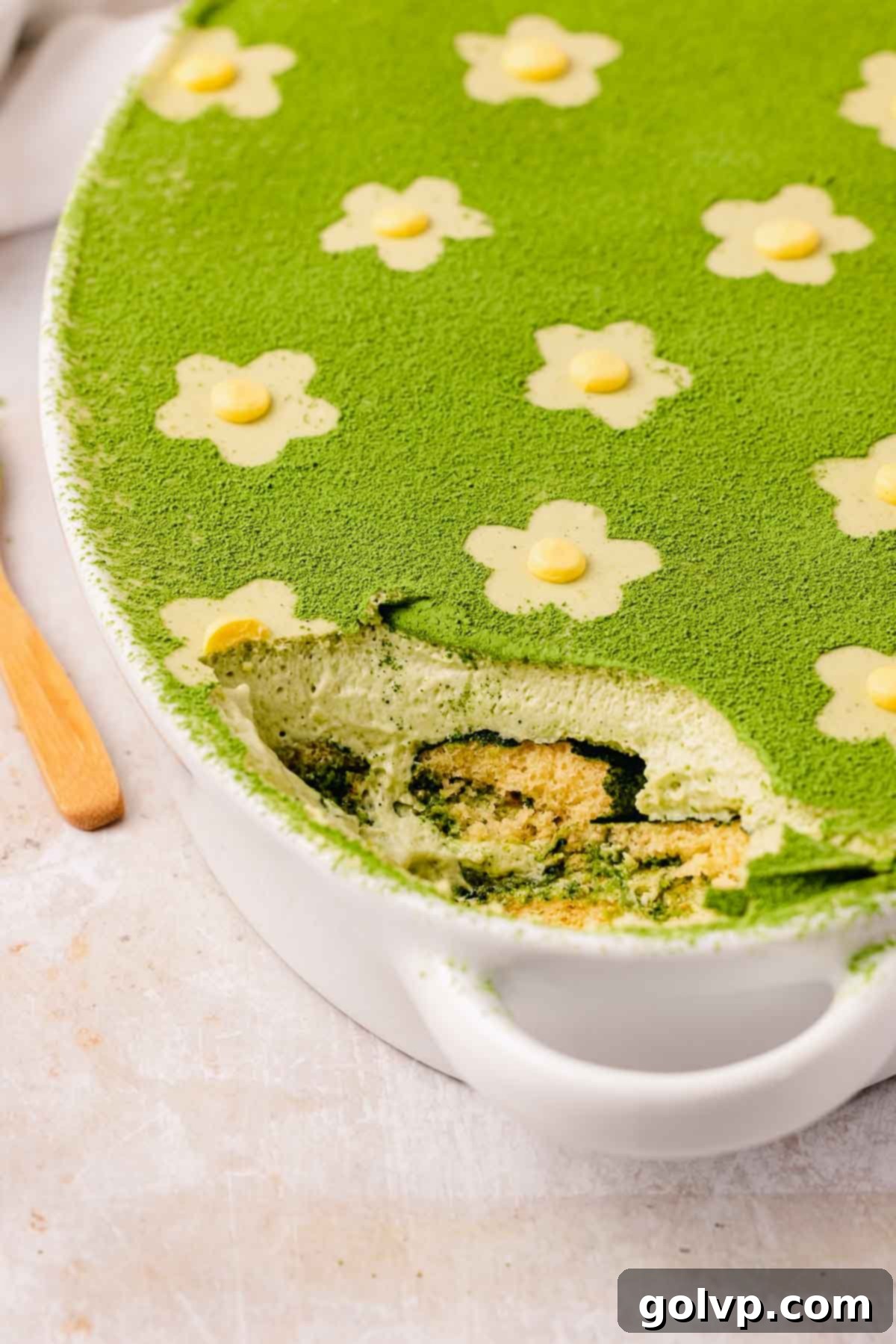 matcha tiramisu with a spoonful removed, decorated with flowers, highlighting its readiness to serve
