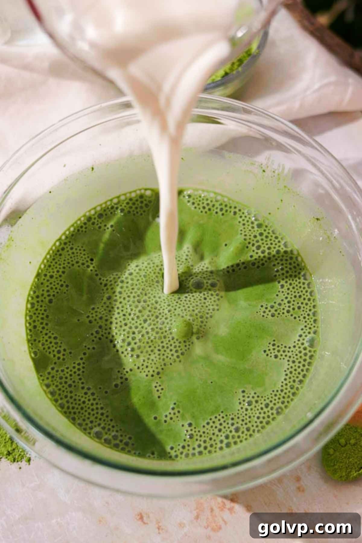Adding fresh milk to the dissolved matcha mixture in a large glass bowl