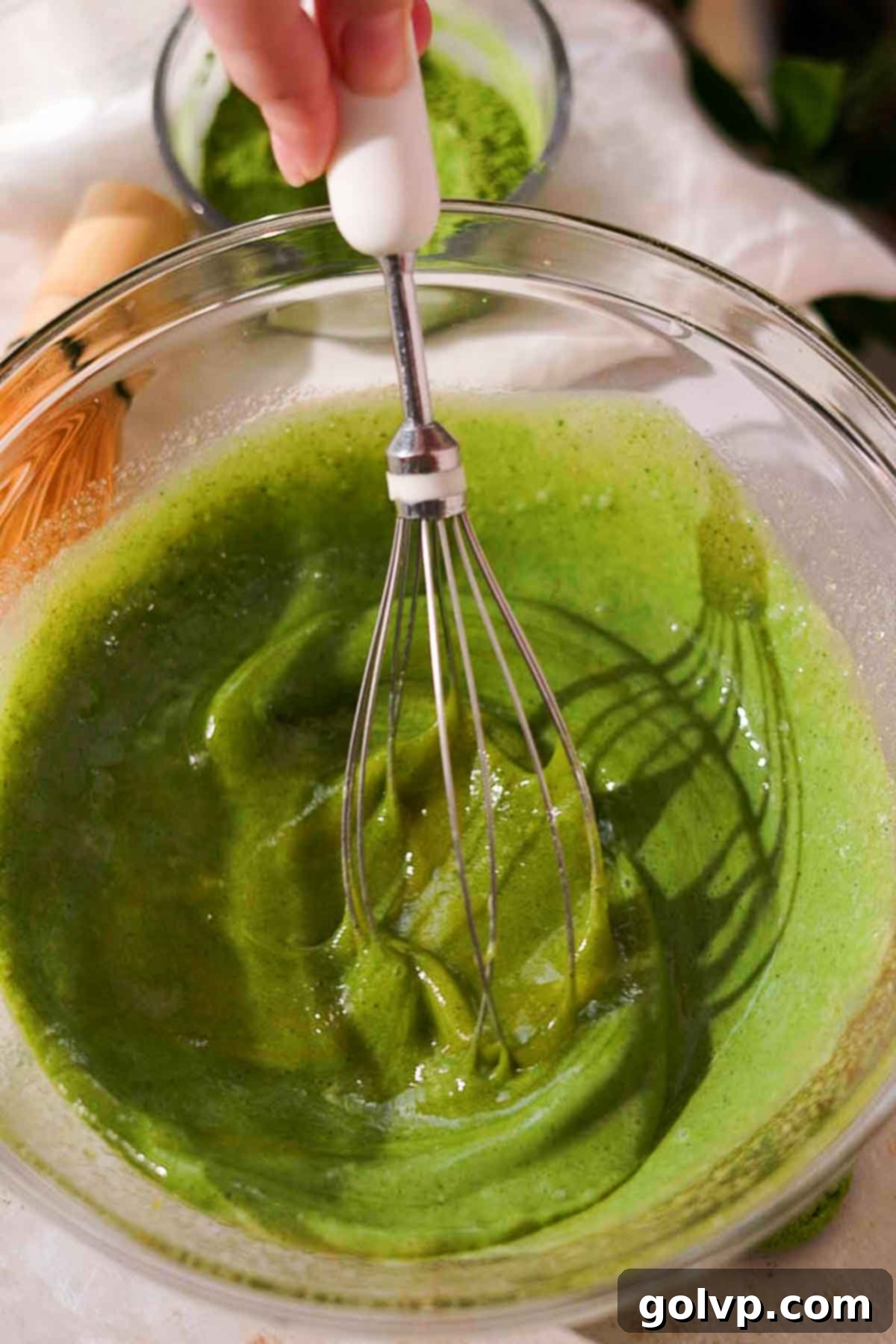 whisking egg yolks, eggs, sugar, vanilla, and matcha milk together in a heat-safe glass bowl