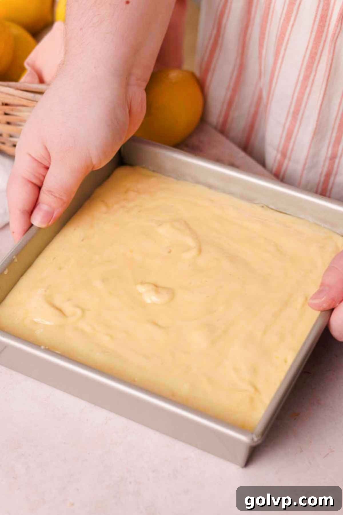 Smooth, pale yellow lemon cake batter gently poured over the arranged lemon slices in a square baking pan, ready for baking.