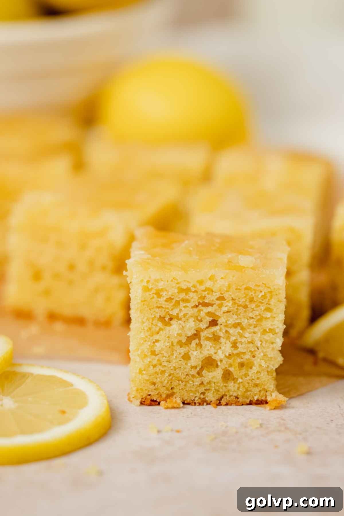 A perfectly square slice of lemon olive oil cake, presented with its vibrant lemon topping and the tender, golden cake beneath.