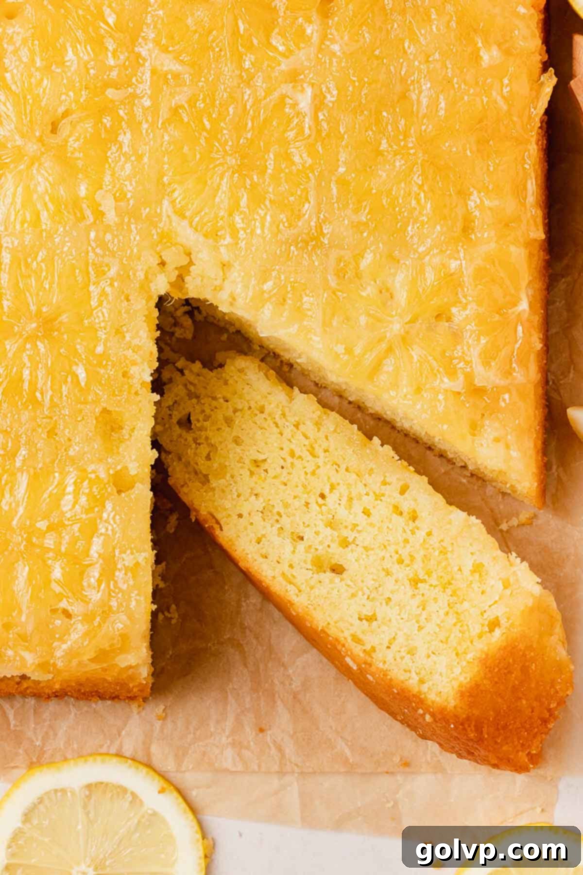 A perfectly sliced lemon olive oil cake, showcasing its tender crumb and a beautiful sticky lemon topping with translucent candied lemon slices.