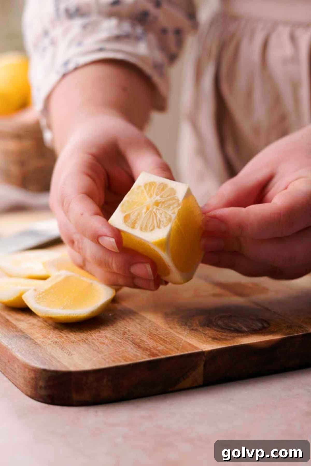 A hand carefully trimming the rind off a lemon, shaping it into a rectangular log for perfect, even slices.